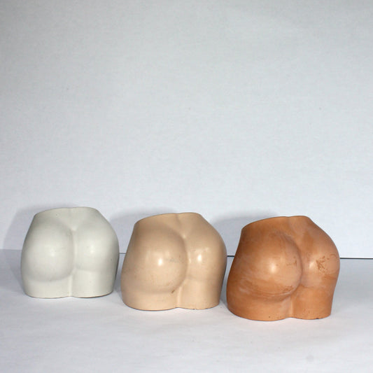 Three concrete bum sculptures of stylized human forms on a white background