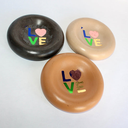 Three round concrete plates with 'LOVE' text and heart designs in rainbow-foiled finish on a white background