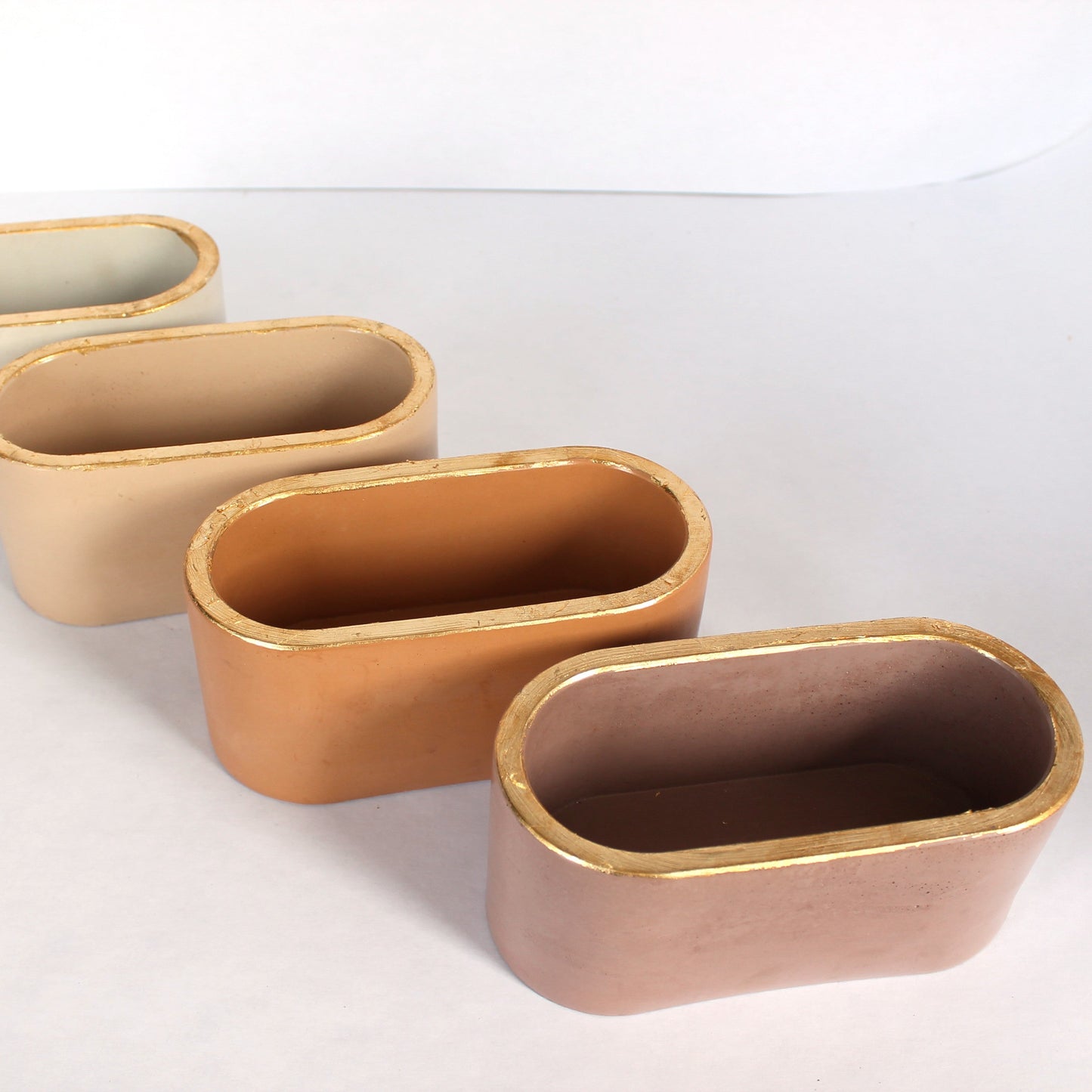 Set of four oval concrete planters in varying shades of brown on a white background