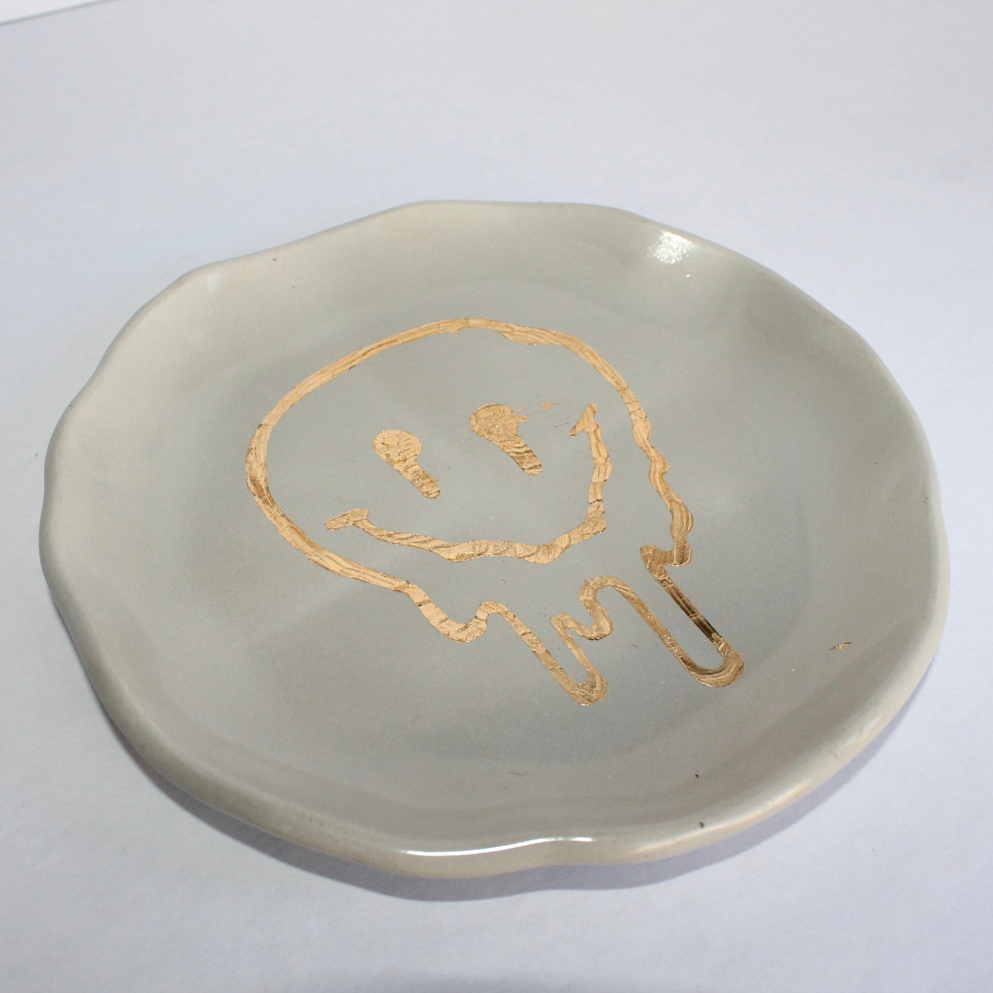 Concrete plate with gold melting smiley design on a white background