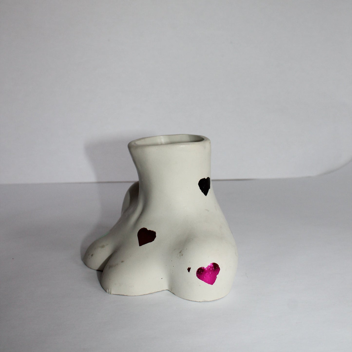White ceramic female body shaped object with color hearts on a light gray background