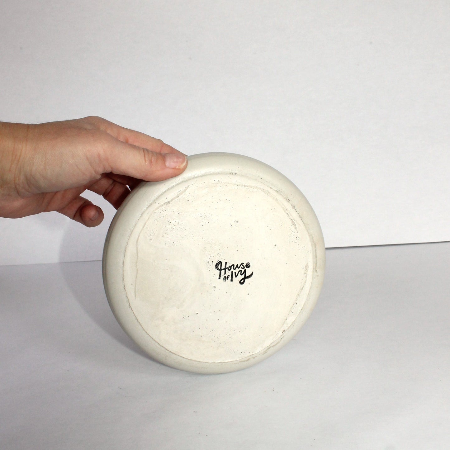 Hand holding a gray concrete plate with 'House of Ivy' branding on a plain background