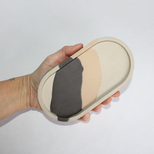 Hand holding a beige and black striped oval-shaped tray against a white background