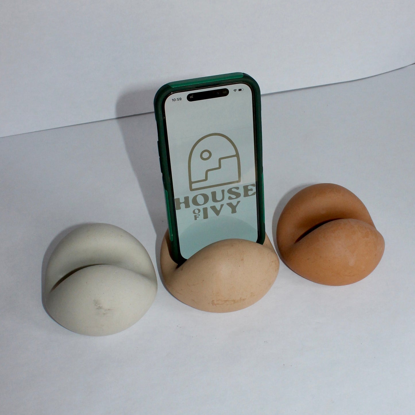 Phone with a screen displaying 'House of Ivy' logo, surrounded by three neutral colored concrete phone stands on a white surface.