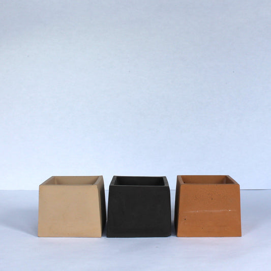 Three small concrete planters in beige, clay, and black on a white background