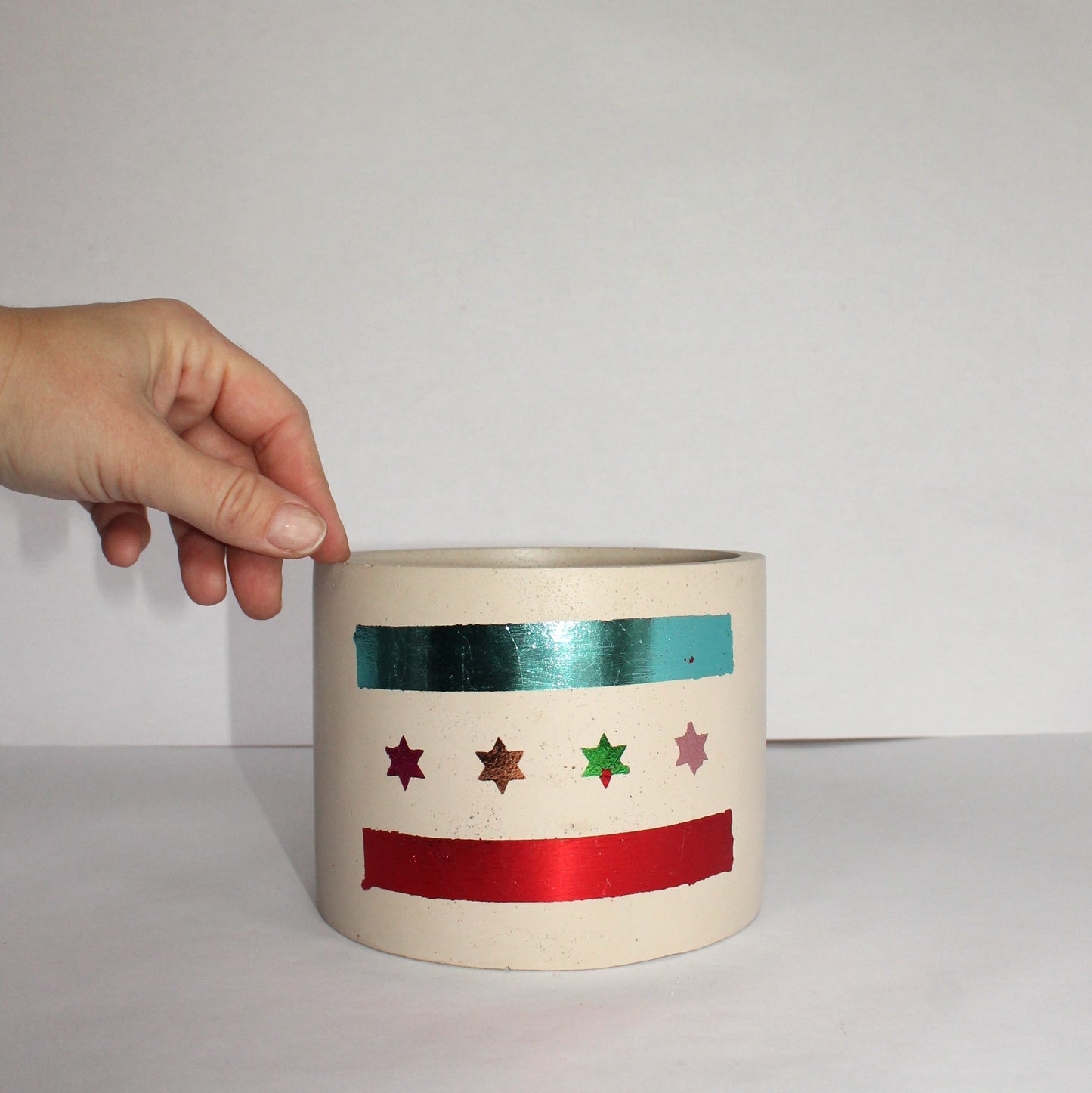 Ceramic pot with colorful Chicago flag held by a hand against a plain background