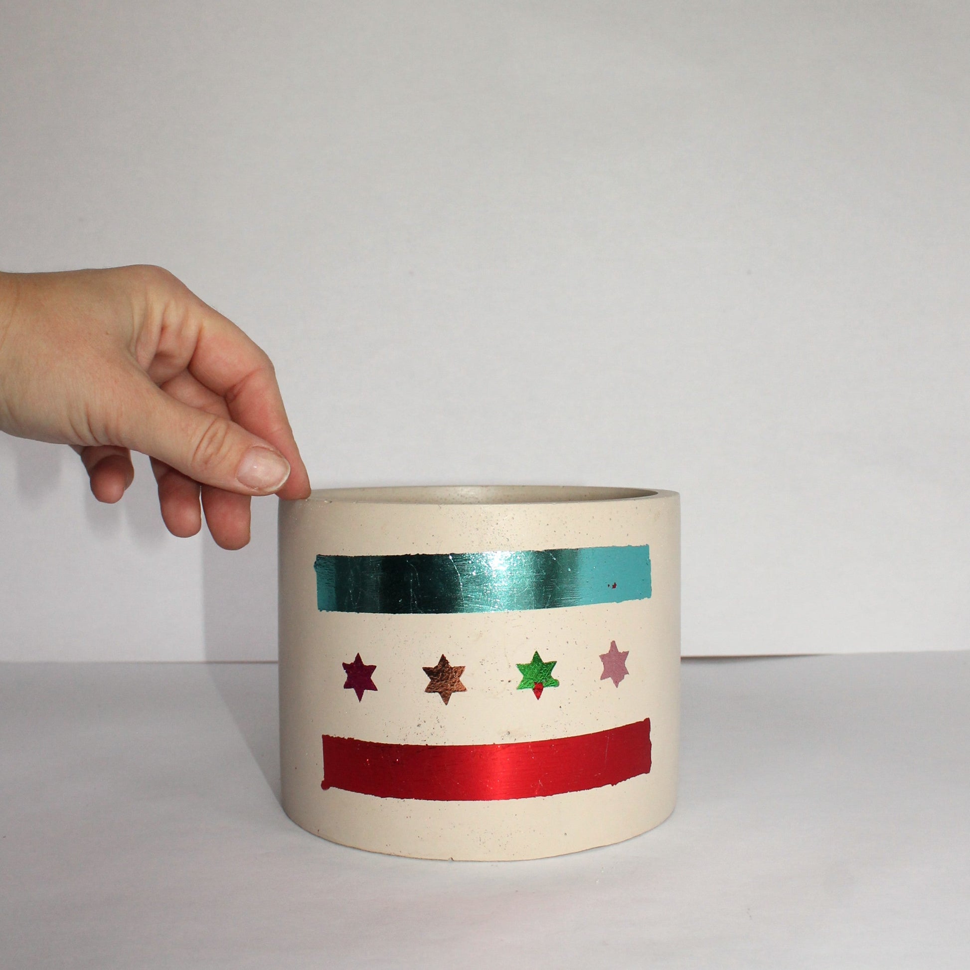 Ceramic pot with colorful Chicago flag held by a hand against a plain background
