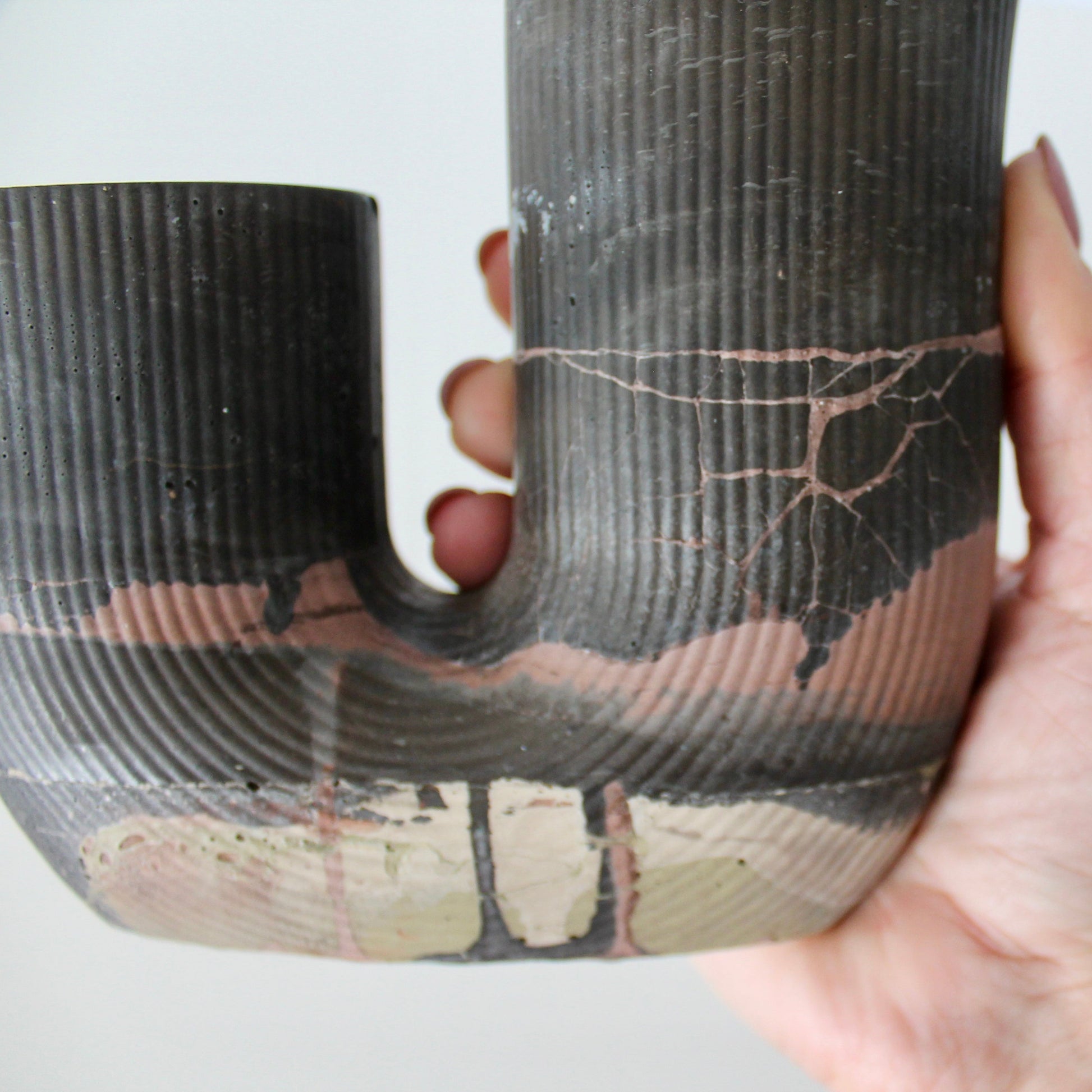 Hand holding a textured concrete vessel against a plain background