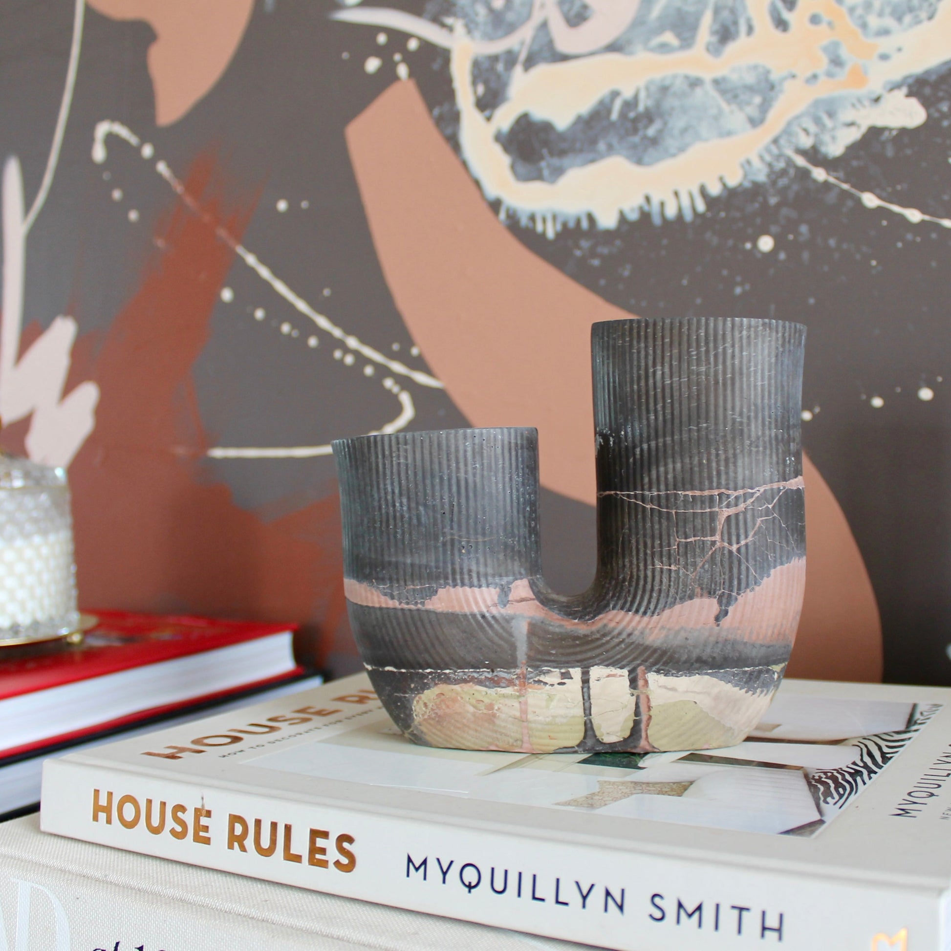 Decorative setup with books, vases, and a candle against a patterned wall.