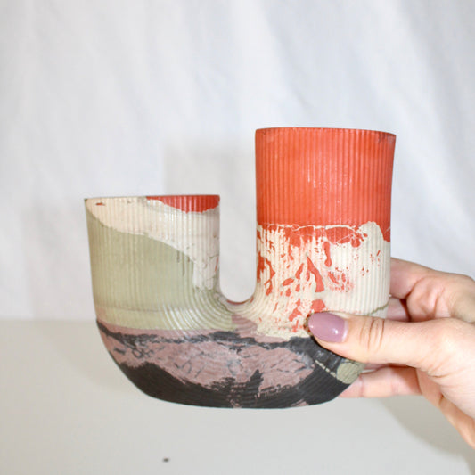 Hand holding a concrete vase with textured surface and color gradient against a plain background