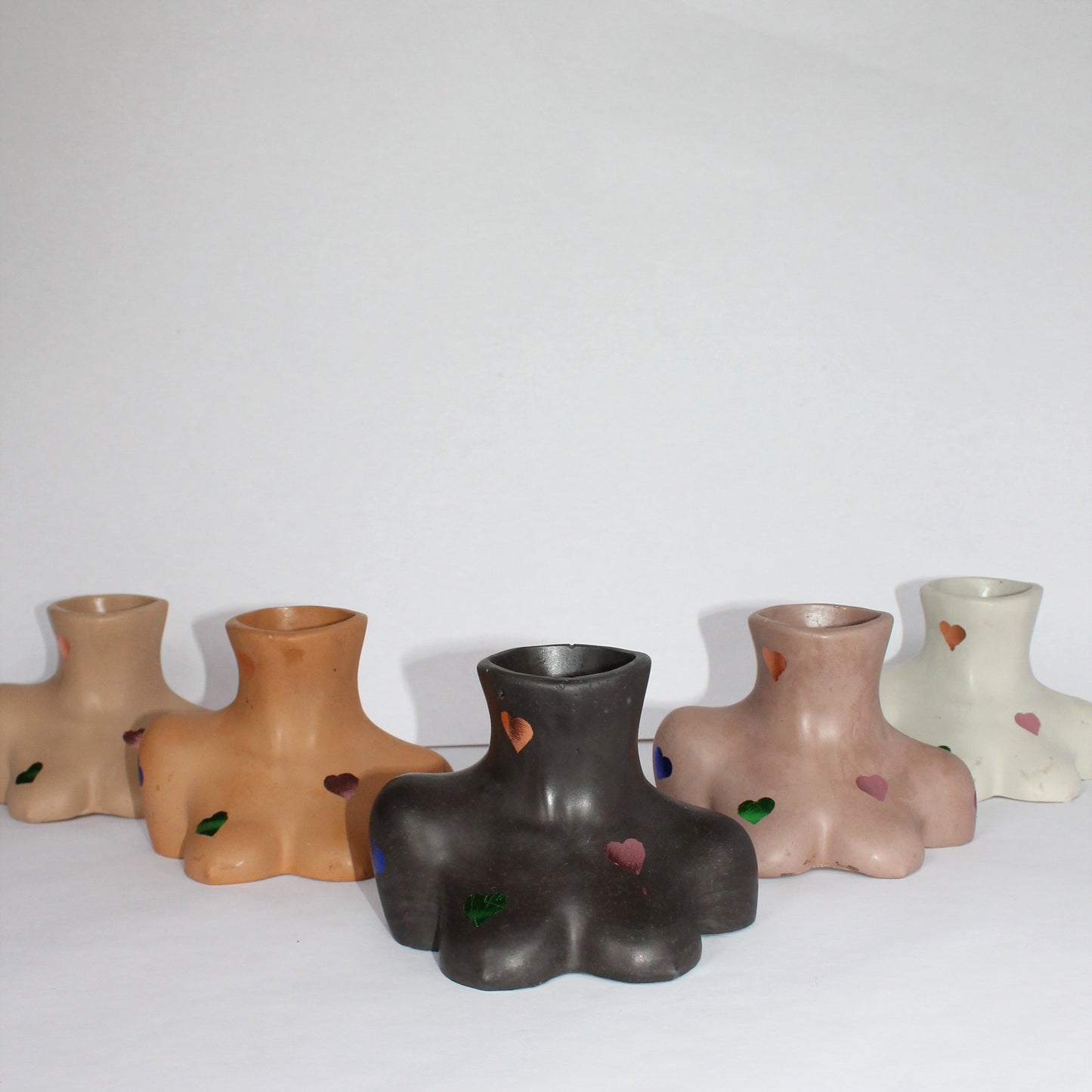 Set of five concrete female body shaped vases in various colors on a white surface