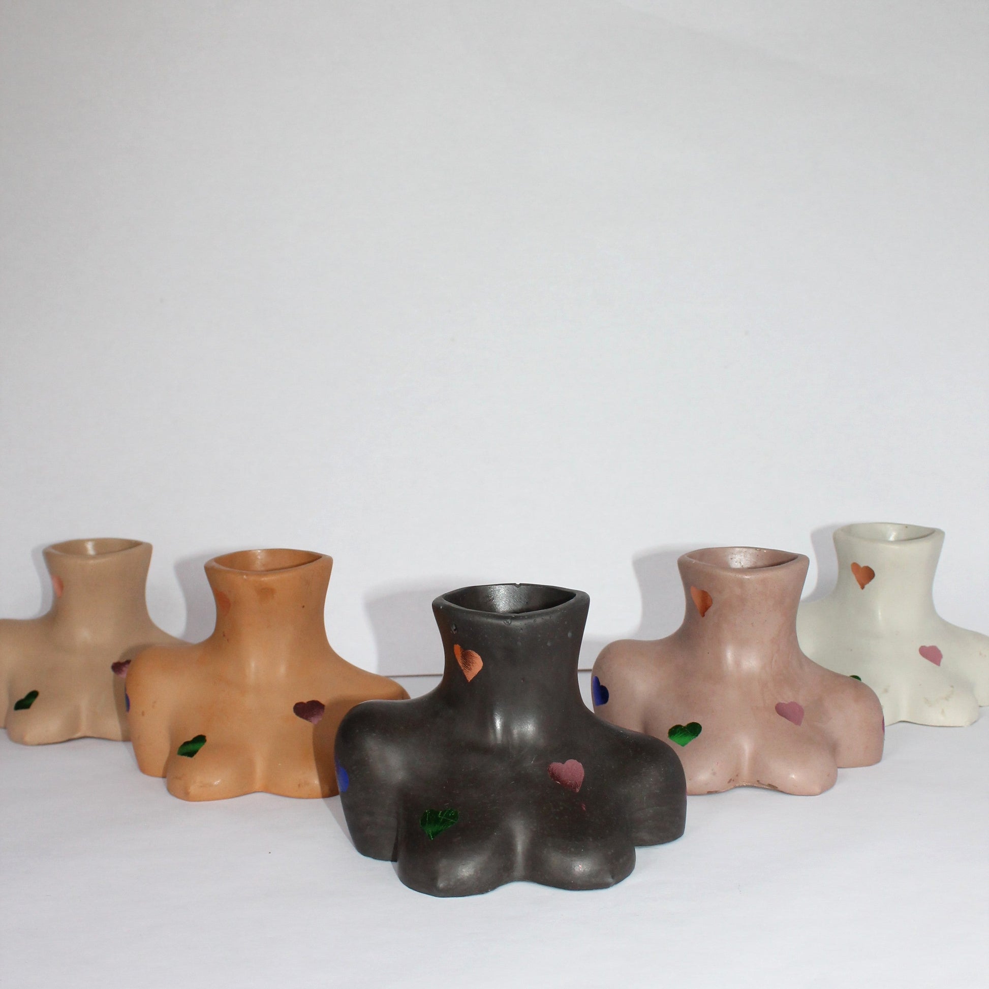 Set of five concrete female body shaped vases in various colors on a white surface