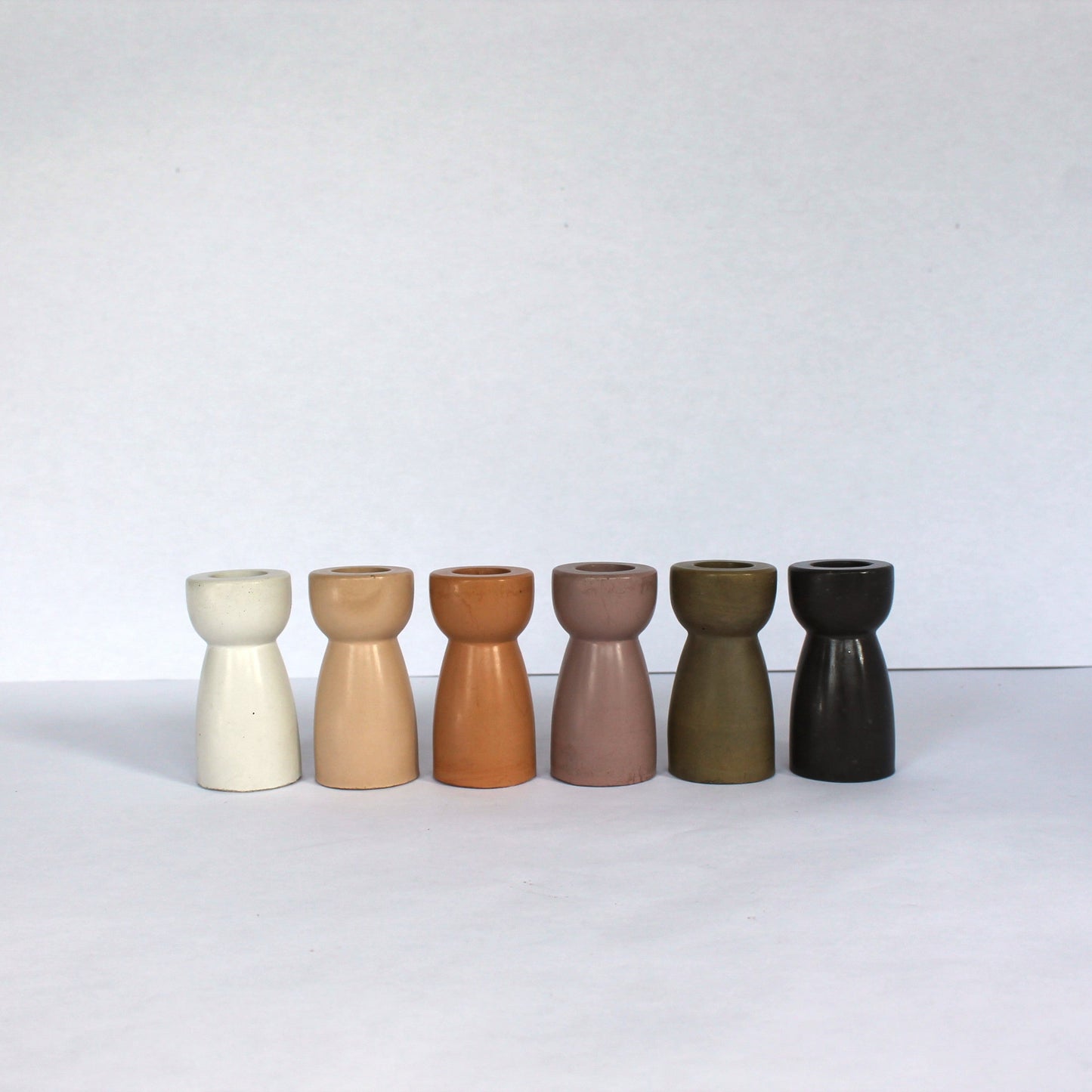 Six concrete candle stick holders in various colors on a white background