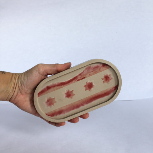 Hand holding a Concrete oval tray with abstract Chicago flag pattern on a white background