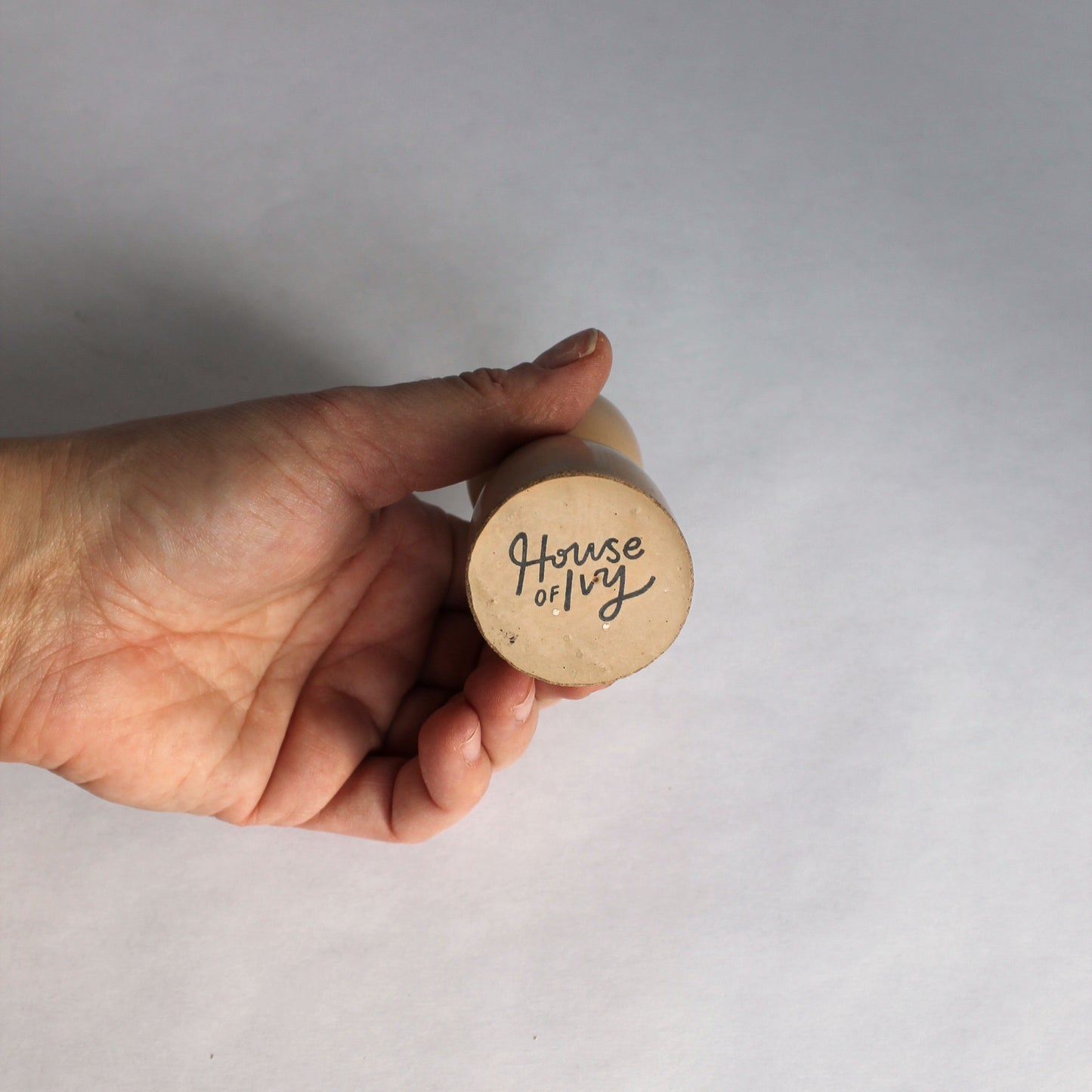 Hand holding a concrete candle holder with 'House of Ivy' branding on a white background