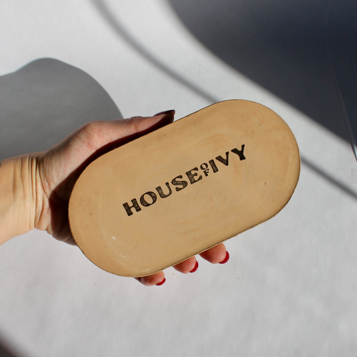 Hand holding a beige oval tray showing the bottom with 'House of Ivy' branding
