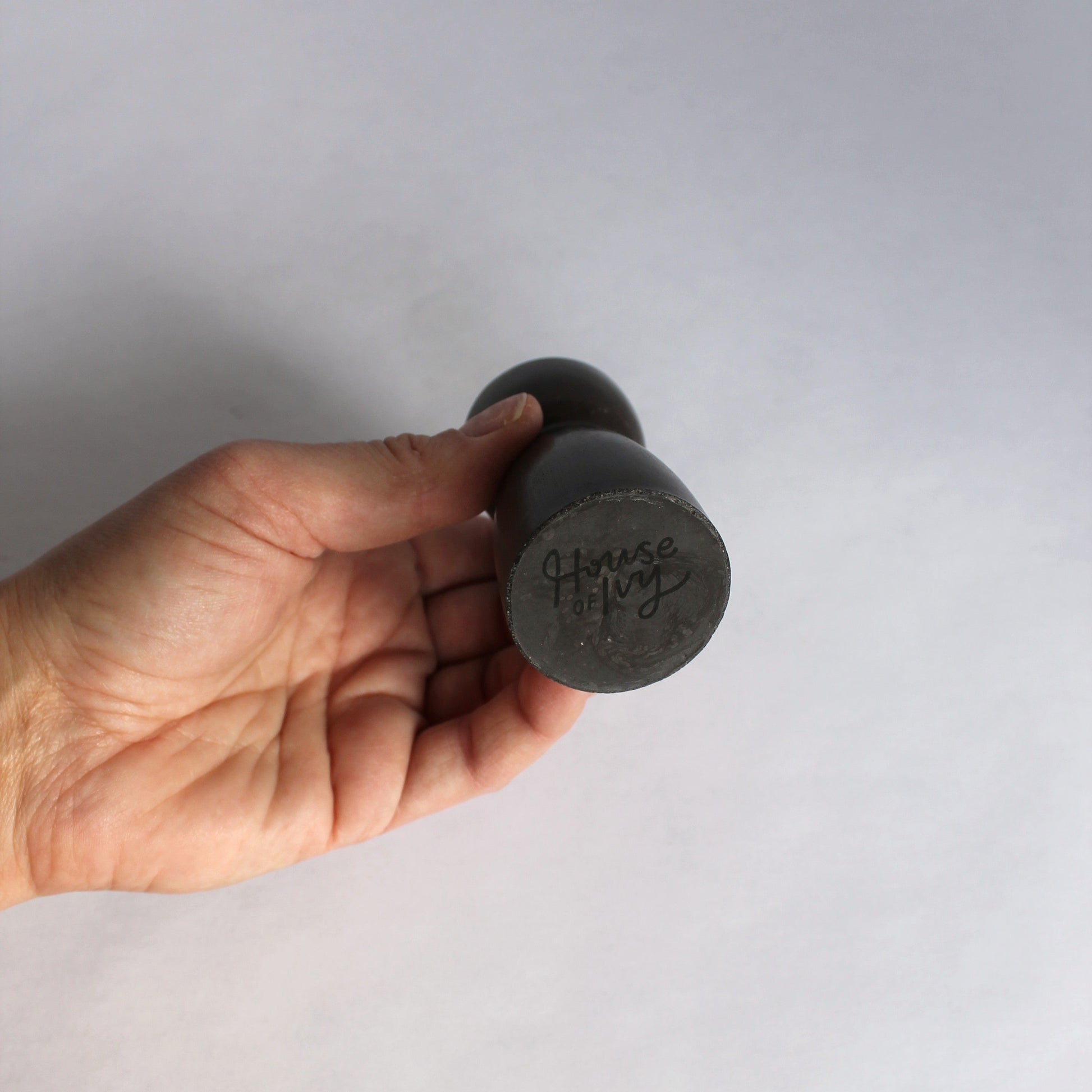 Hand holding a black candle stick holder with 'House of Ivy' branding on a white background