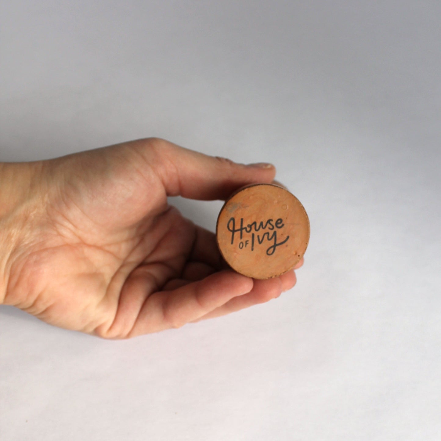 Hand showing bottom of concrete candle stick holder with 'House of Ivy' on a white background