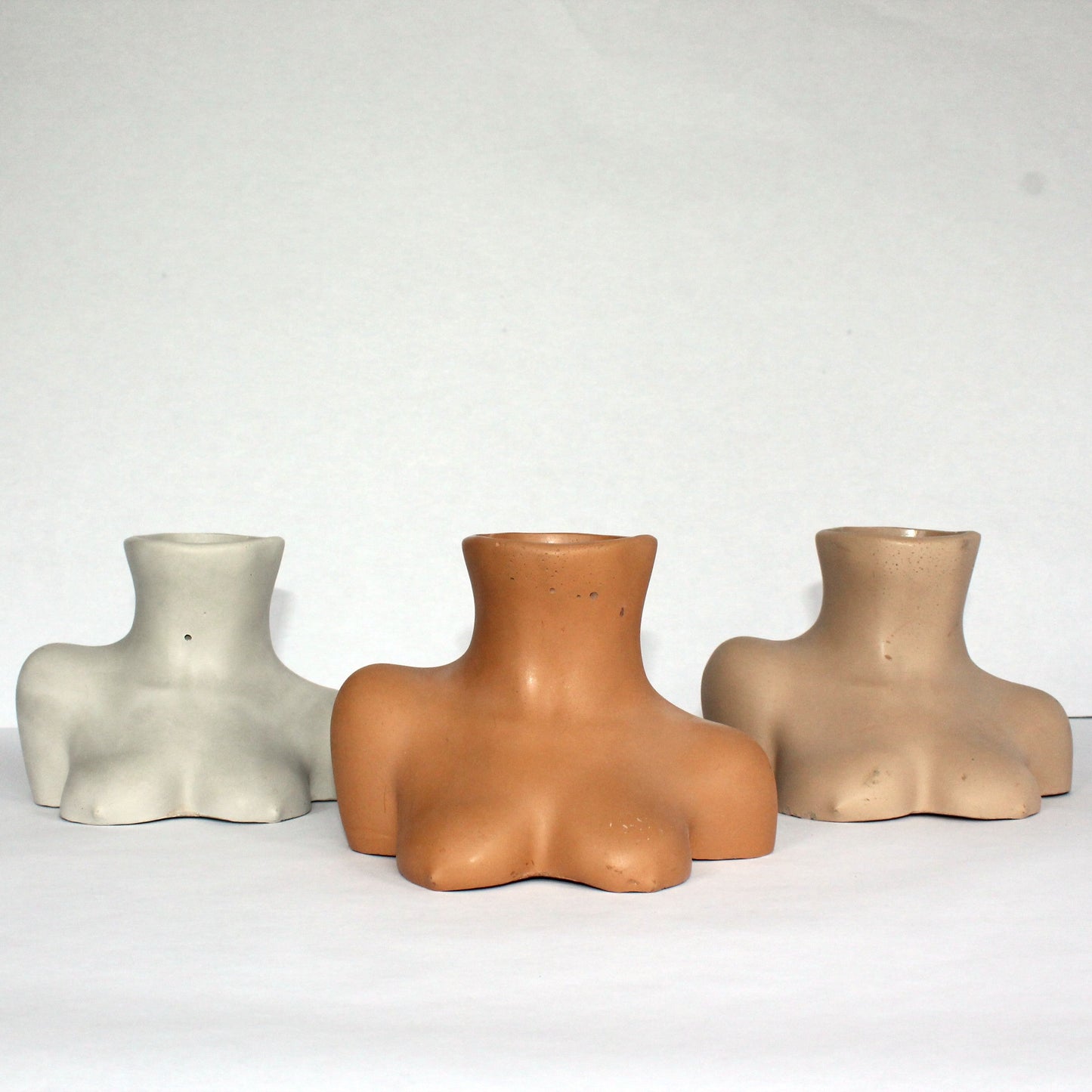 Three concrete busts in different neutral colors on a white background
