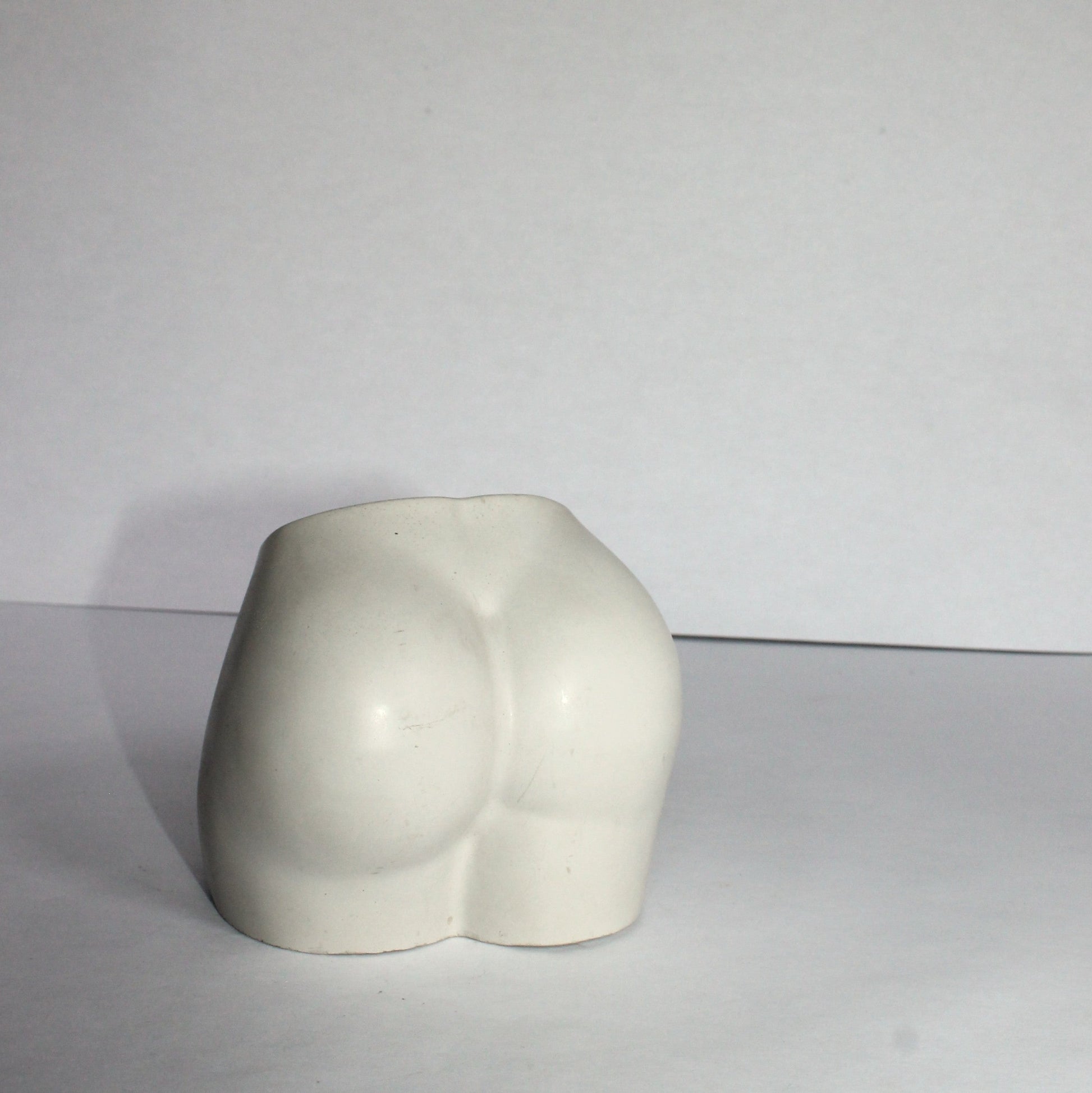 light gray concrete sculpture of a torso on a white surface with a white background