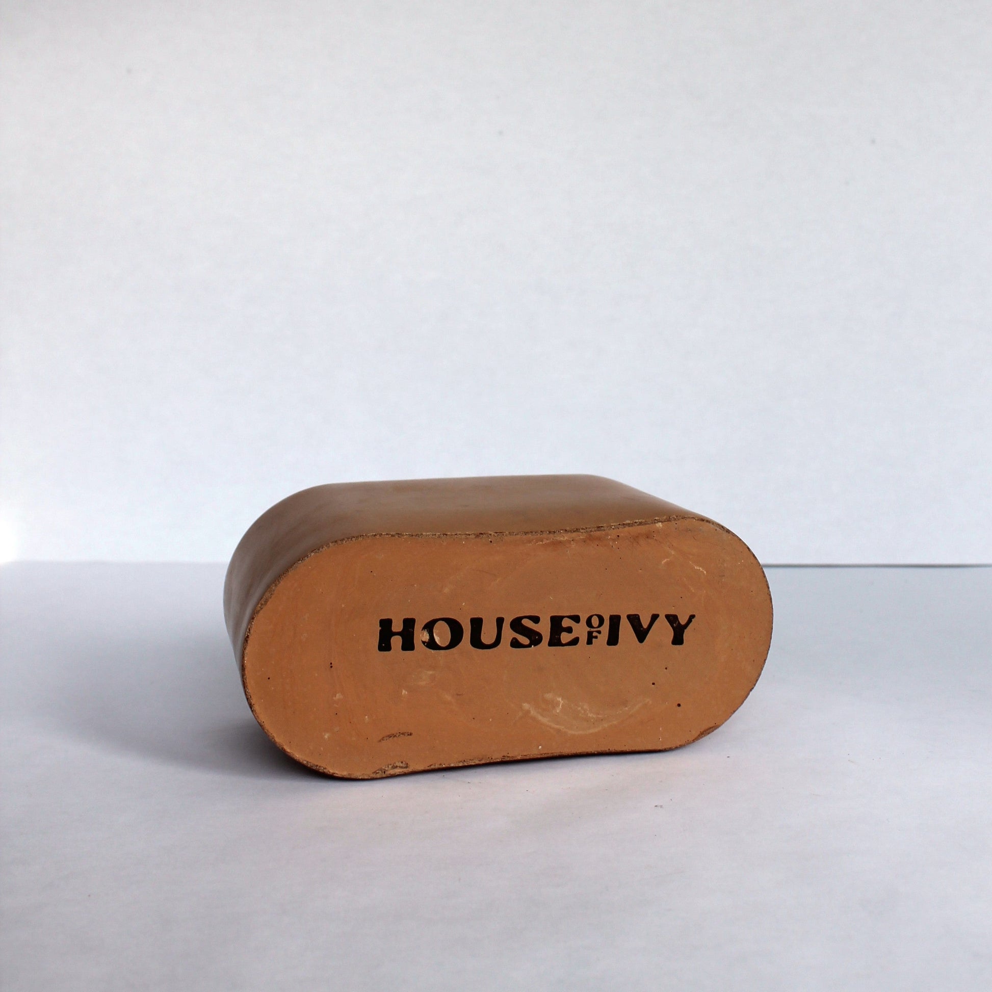 Bottom of clay colored concrete dish with 'HOUSE OF IVY' branding on a white background