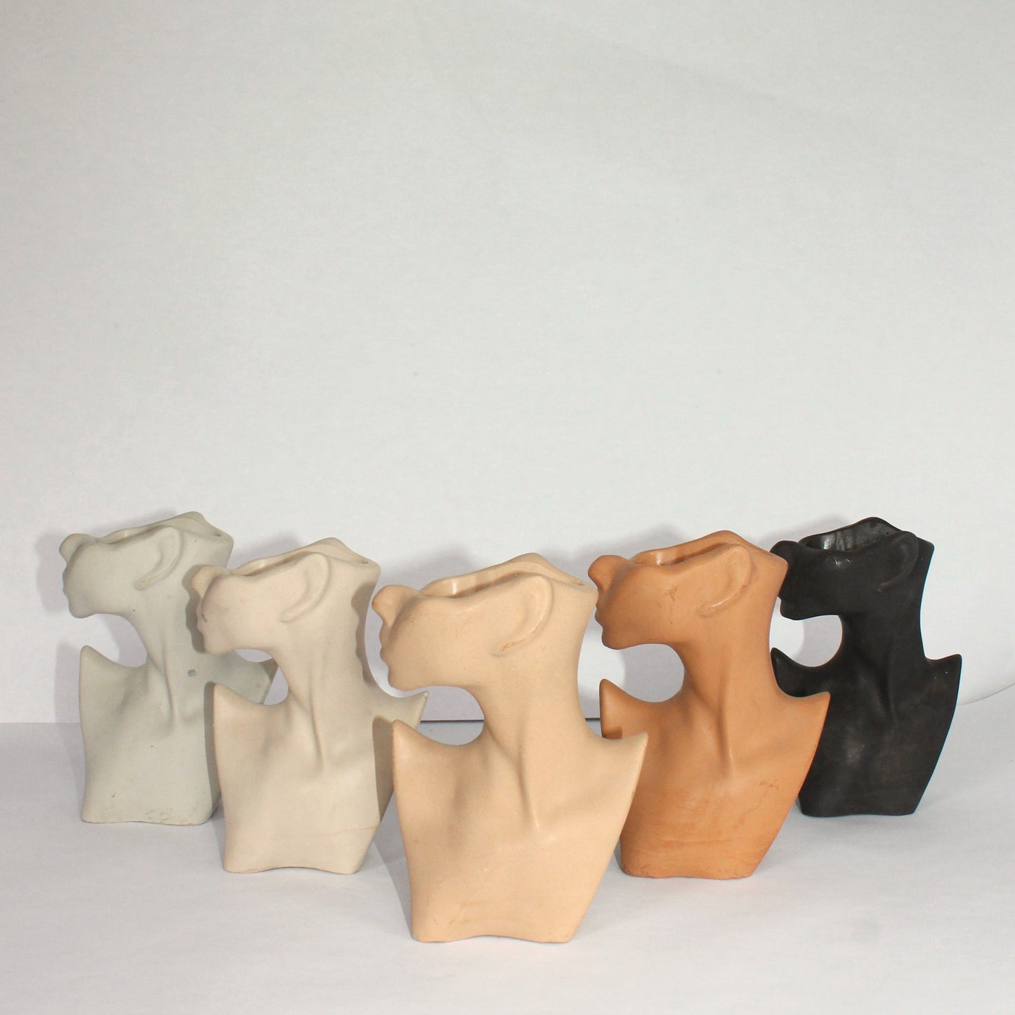 Five concrete female body shaped pieces in different neutral colors on a white surface.