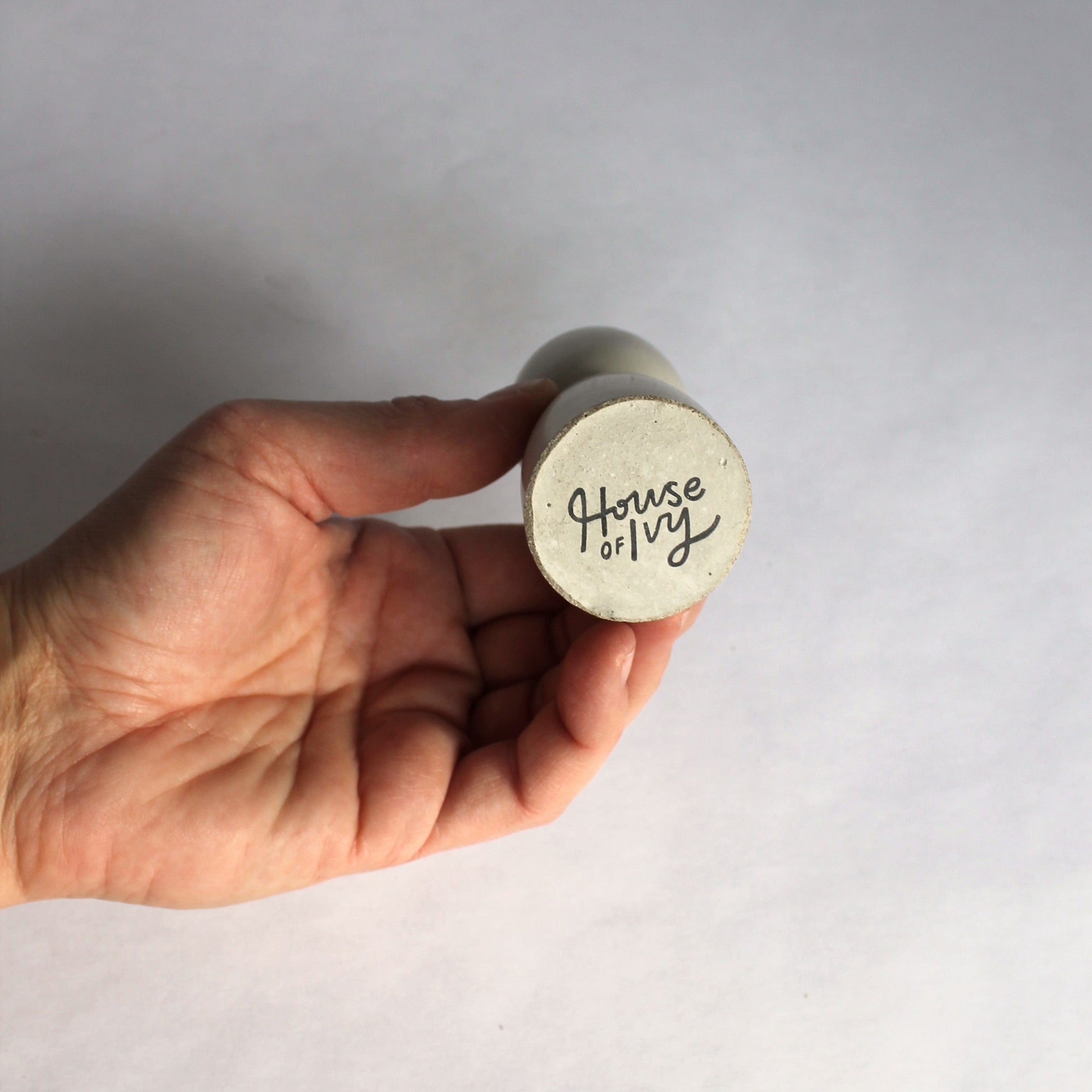Hand holding a candle holder with 'House of Ivy' branding against a plain background