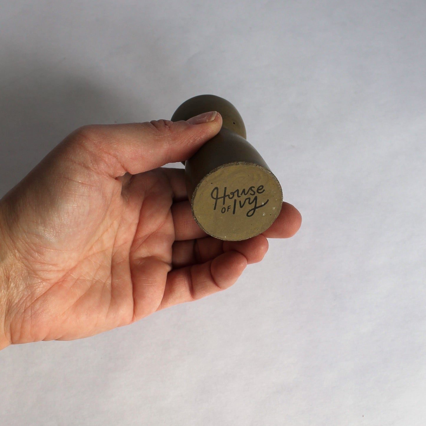 Hand holding a concrete candle holder with 'House of Ivy' branding on a plain background