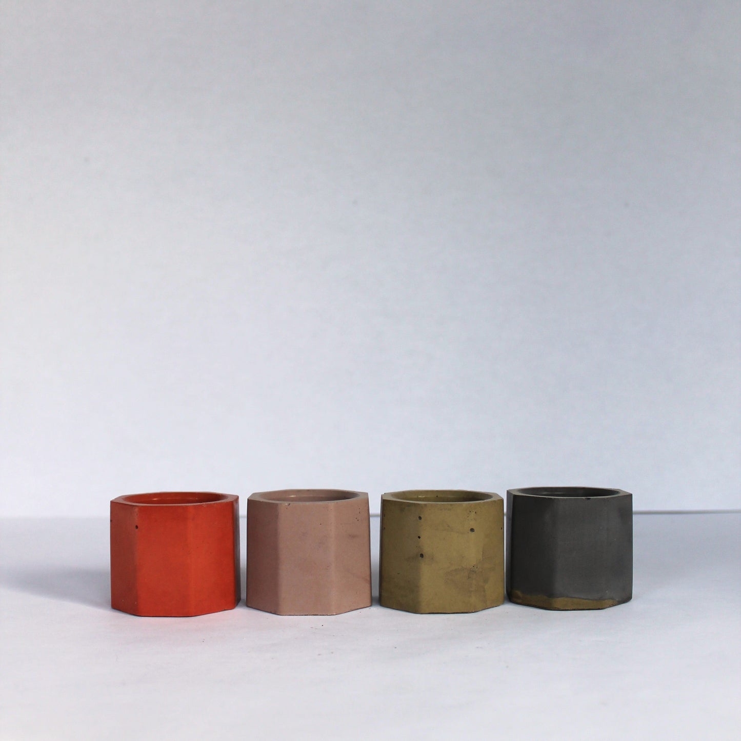 Four cylindrical small concrete pots in different colors on a white background