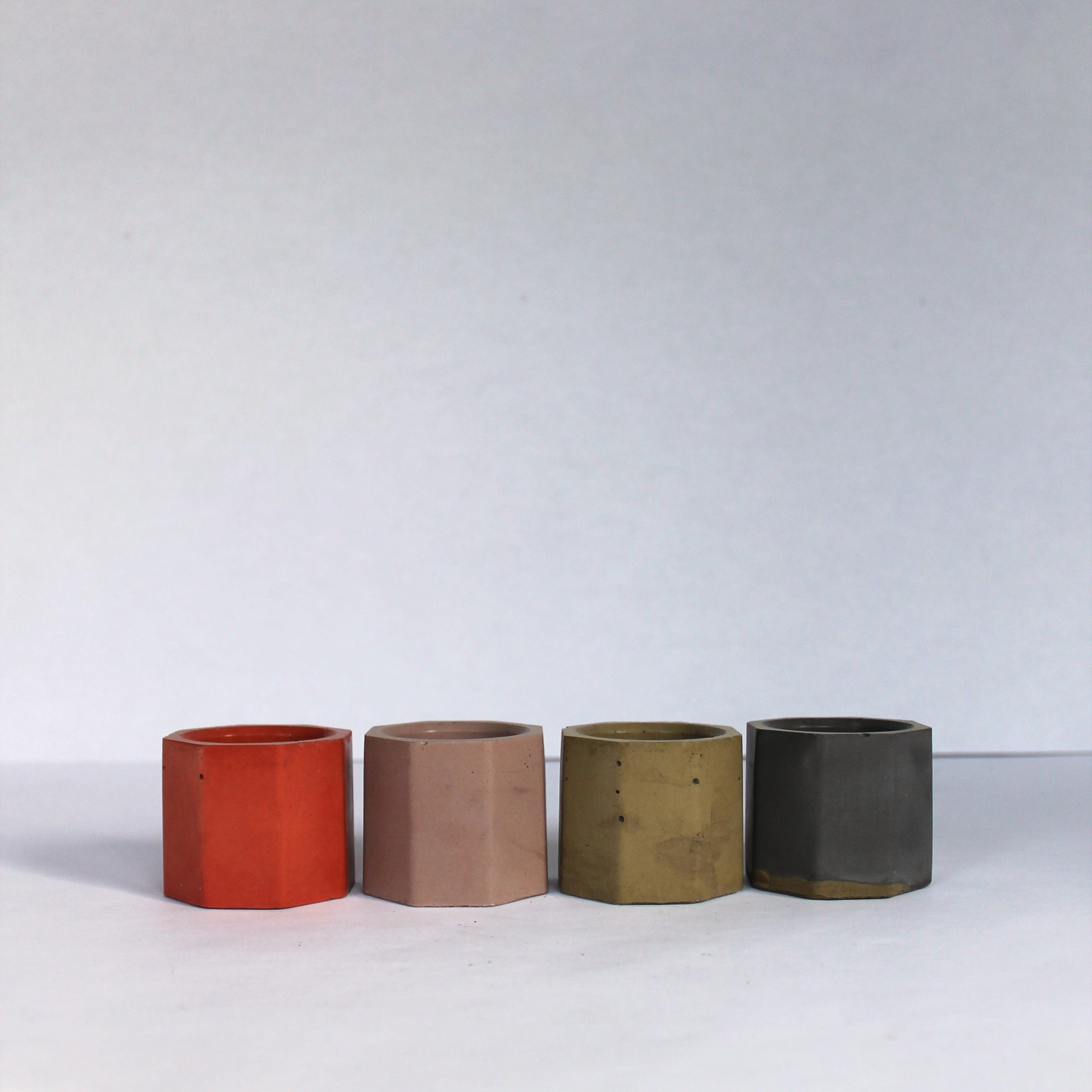Four cylindrical small concrete pots in different colors on a white background