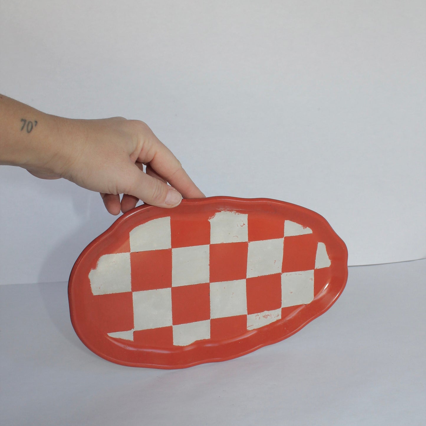 Hand holding an orange and white checkered plate against a white background