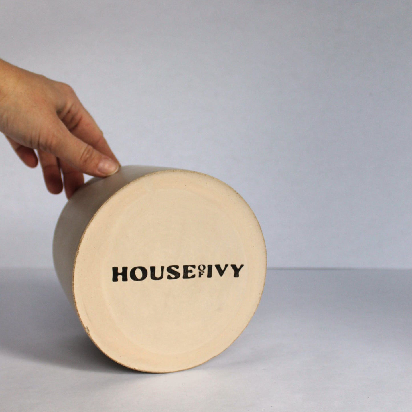 Bottom of round concrete pot with 'House of Ivy' branding on a white background