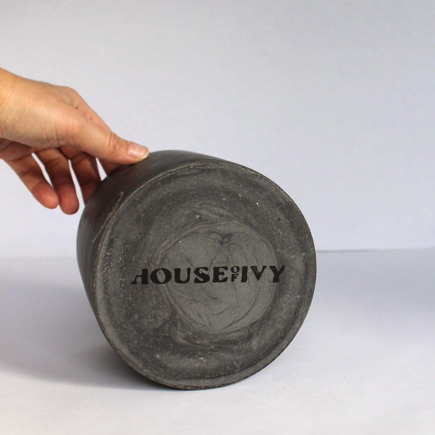 Hand holding a dark gray container with 'House of Ivy' branding on a white background