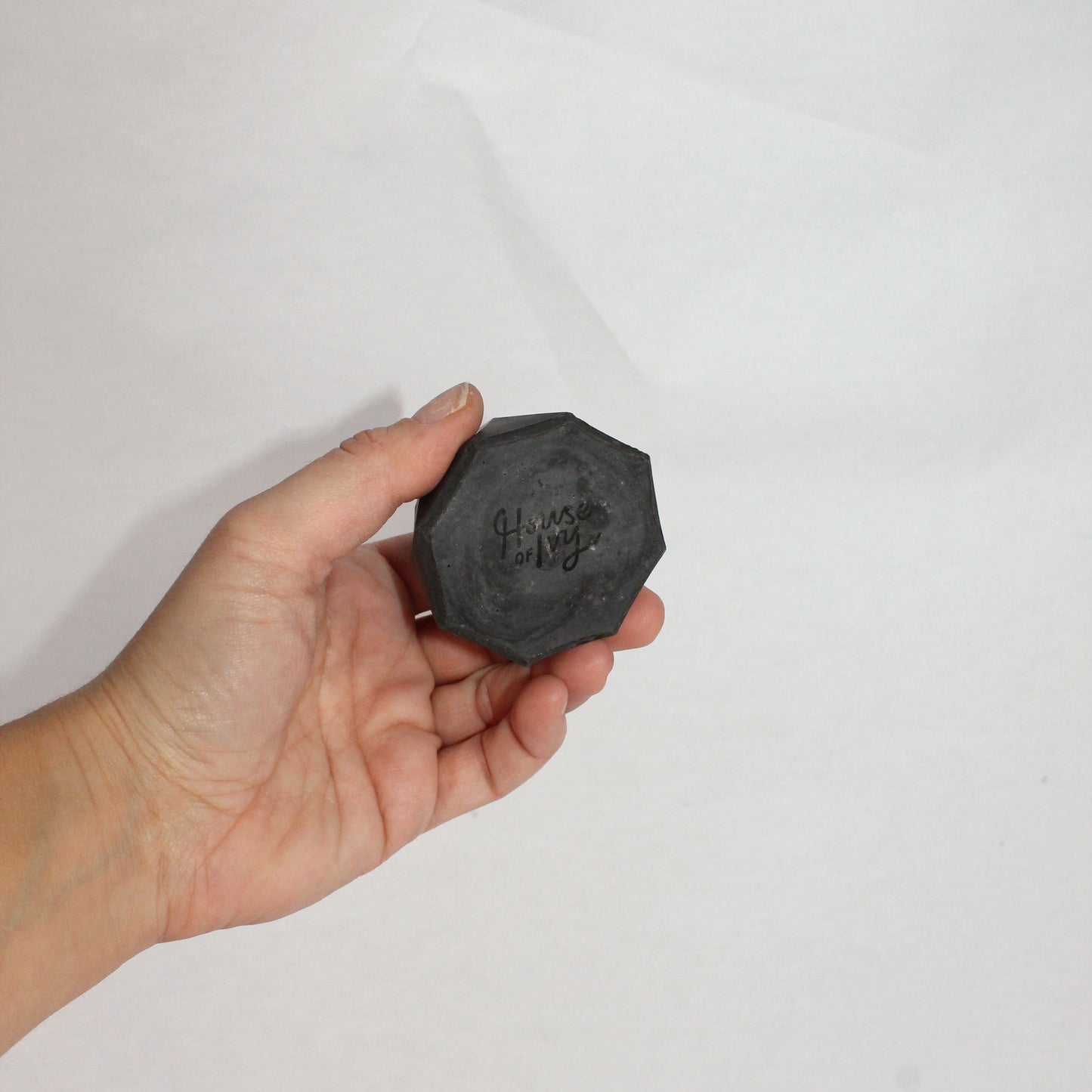 Hand holding a black hexagonal concrete dish against a white background