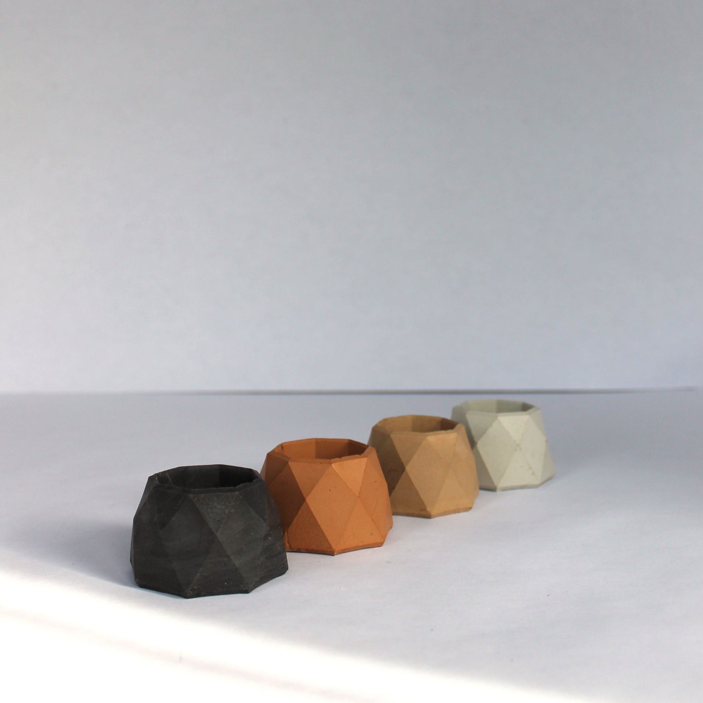 Five geometric concrete jewelry dishes in various neutral colors on a white surface with a white background