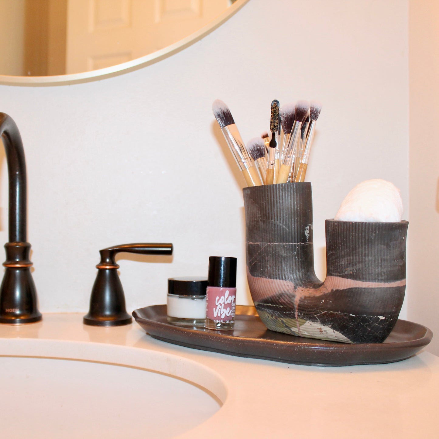 Bathroom sink with black faucet and makeup brushes in holder on the counter