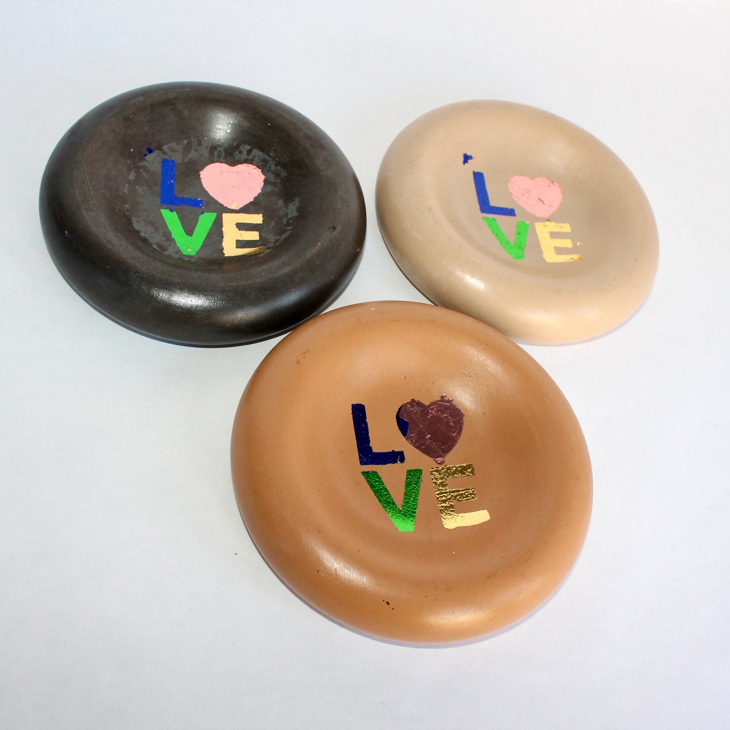 Three round concrete plates with 'LOVE' text and heart designs in rainbow-foiled finish on a white background