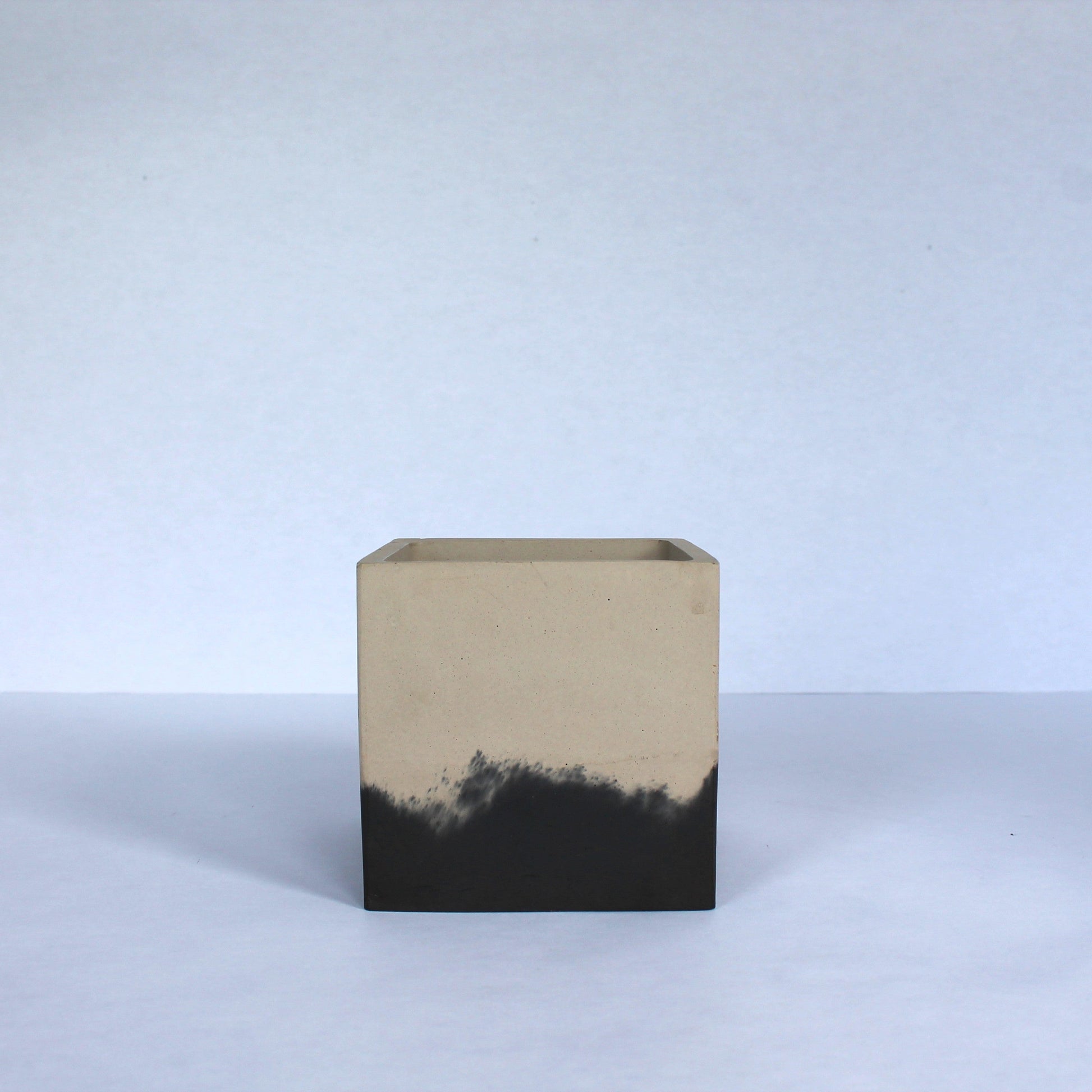 Square concrete planter with two-toned beige and black design on a white background