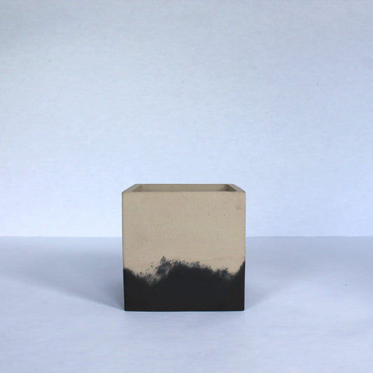 Square concrete planter with two-toned beige and black design on a white background