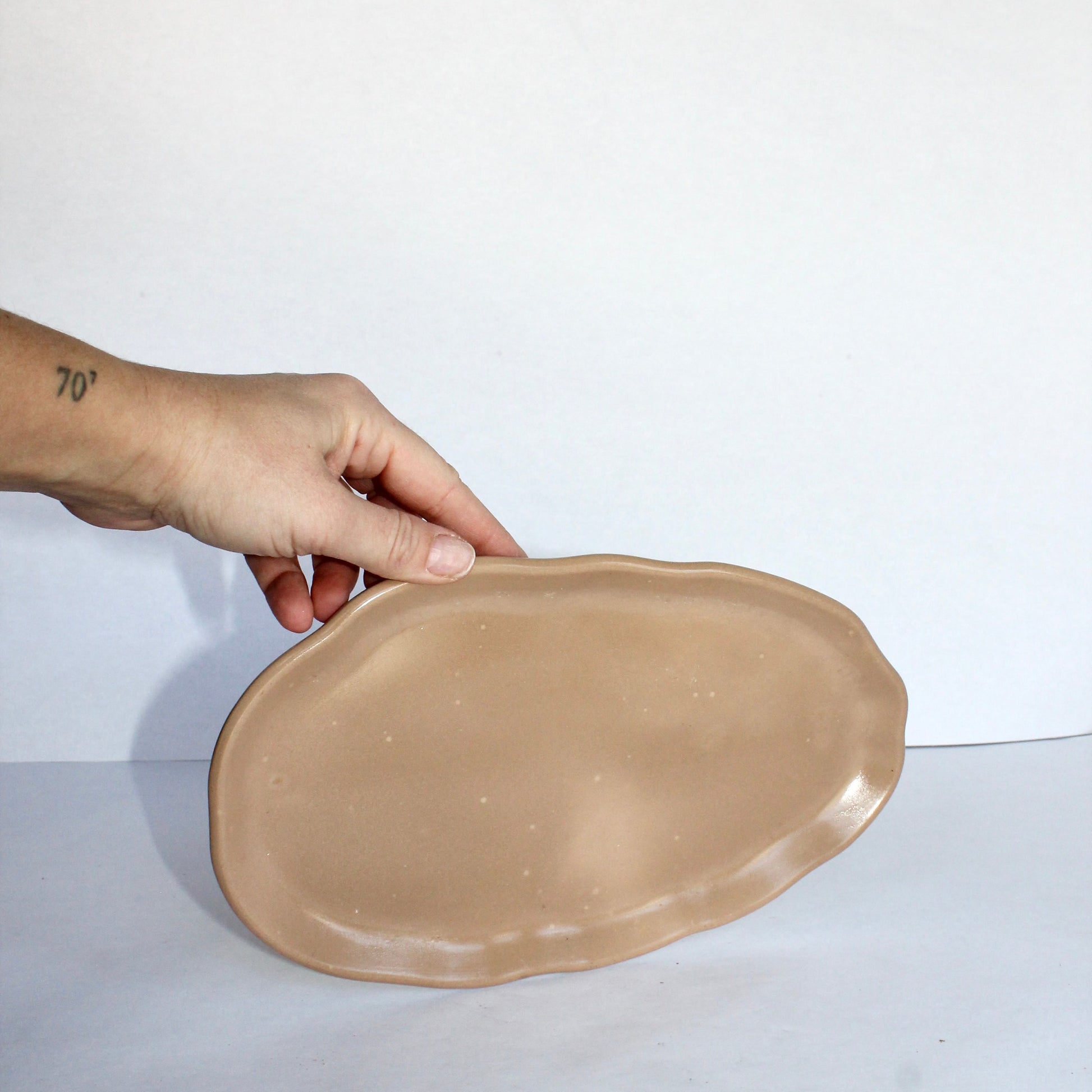 Hand holding a beige concrete plate on a white background