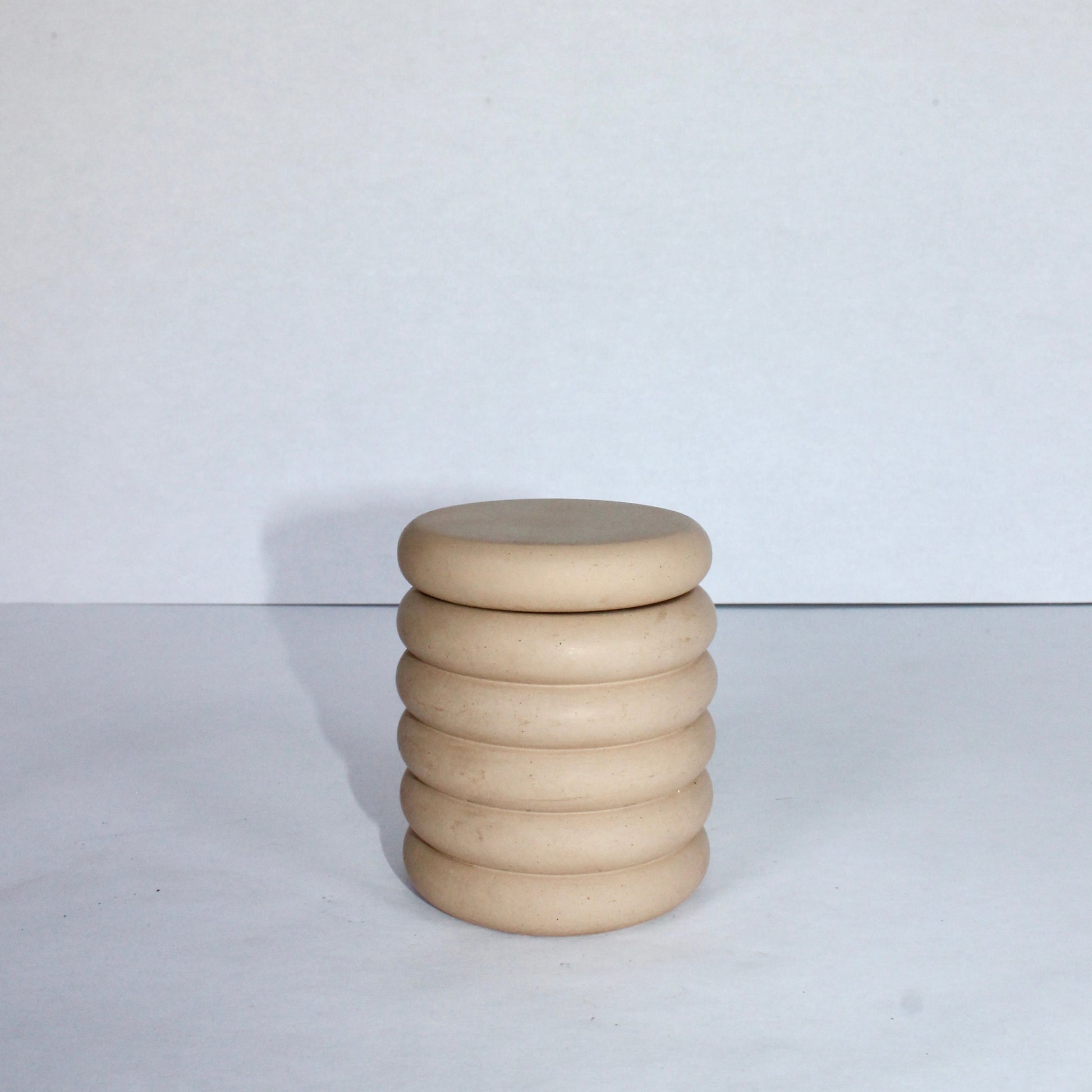 Beige concrete jar with a lid on a white surface and background
