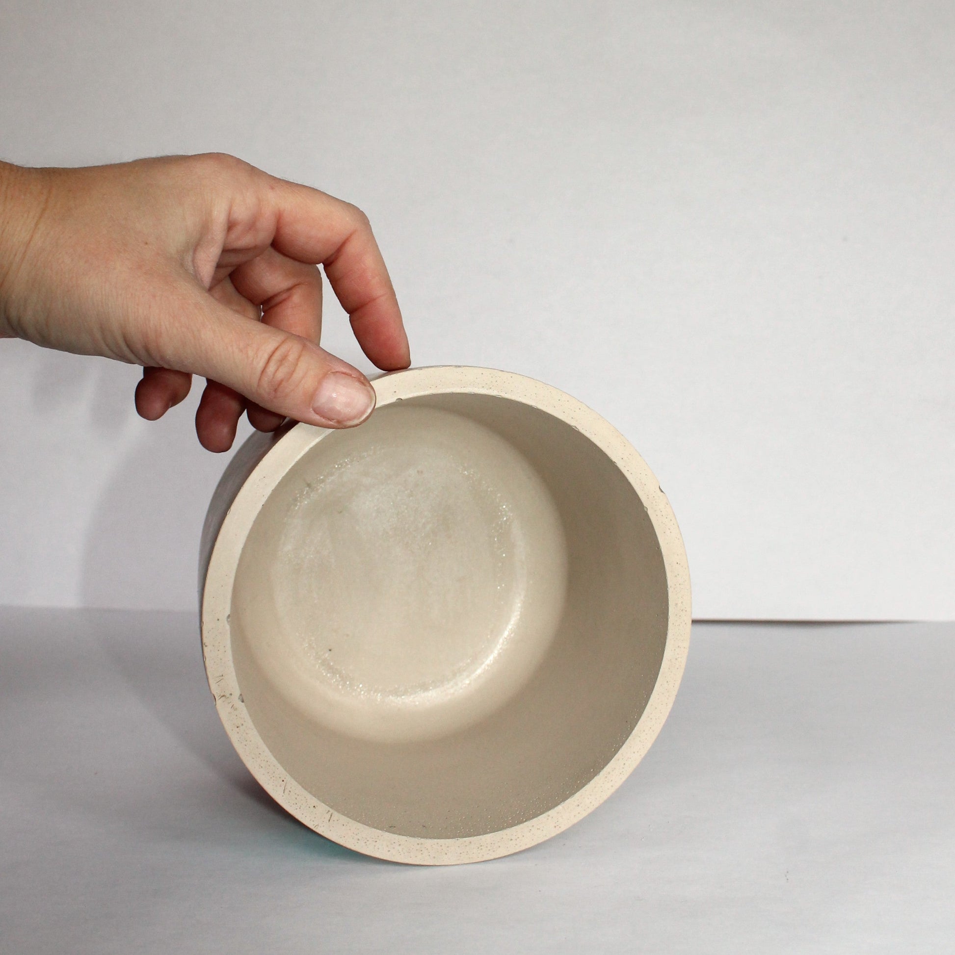 Hand holding a beige ceramic bowl against a white background
