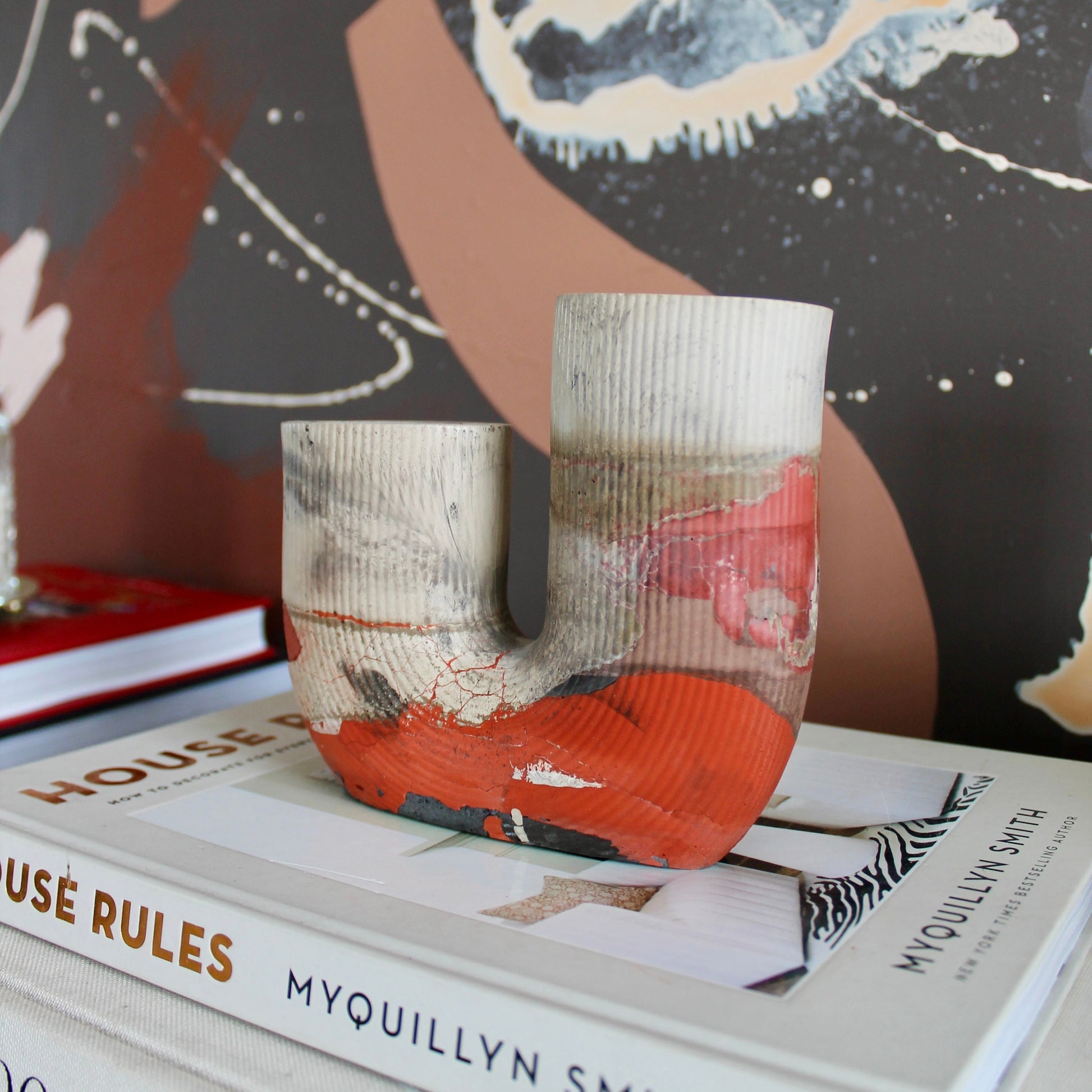 Decorative vase with abstract design on top of books against a colorful abstract painting background