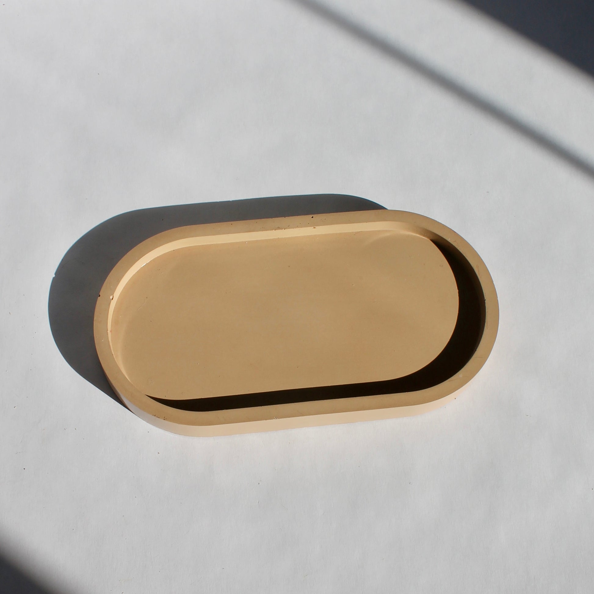 An oval-shaped concrete tray in a beige color, displayed on a white surface with shadow play.