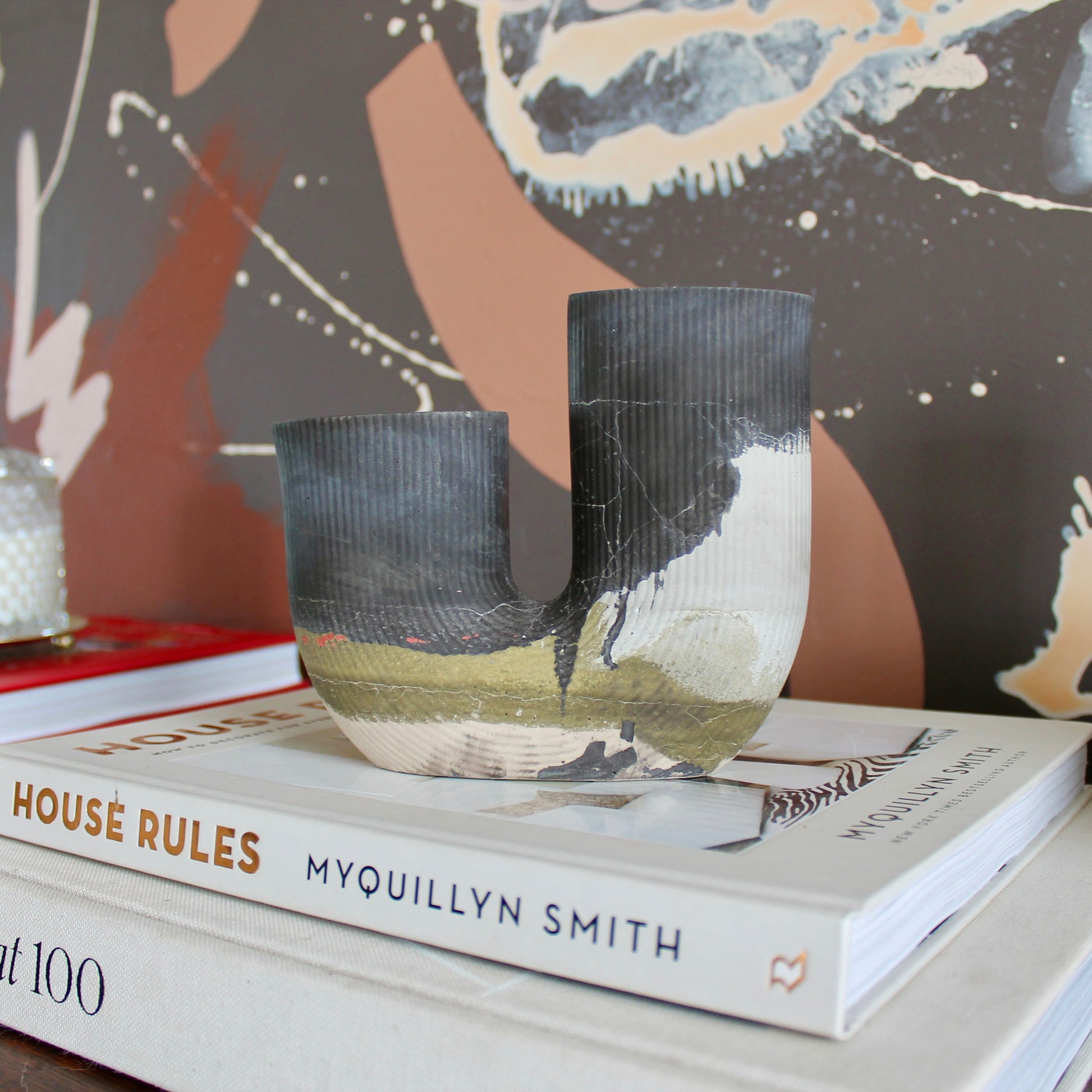 Stack-of-books-on-a-surface-with-cement-vessel-and-other-decorative-elements-in-the-background