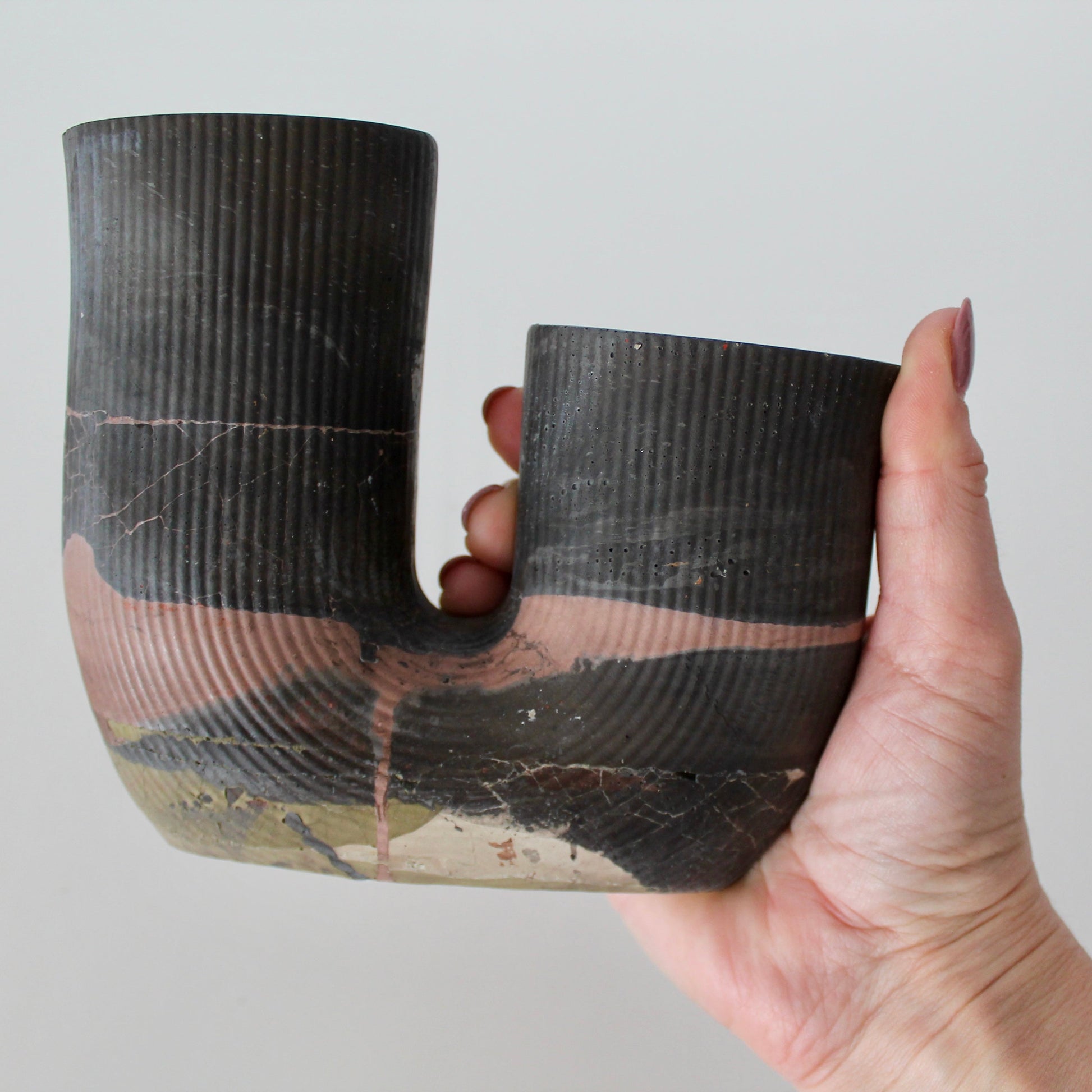 Hand holding a black cement U-shaped vase against a plain background