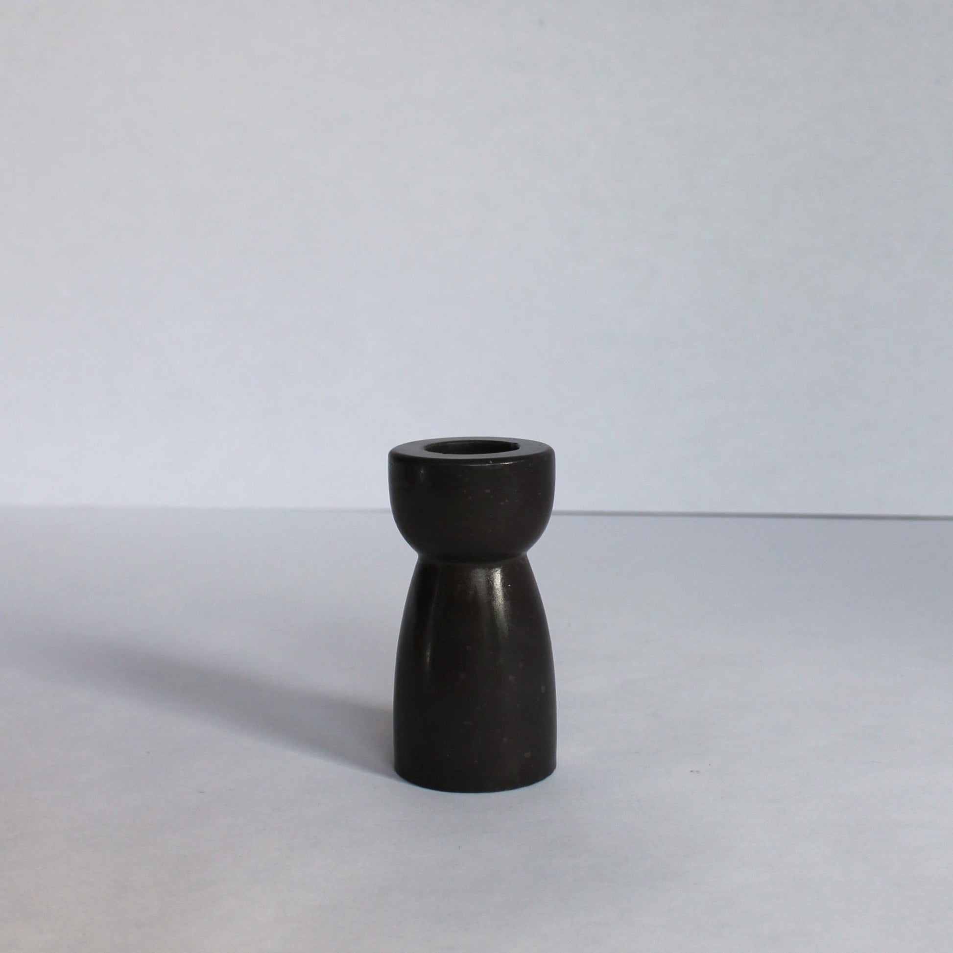 Black concrete candle stick holder on a white surface with a white background