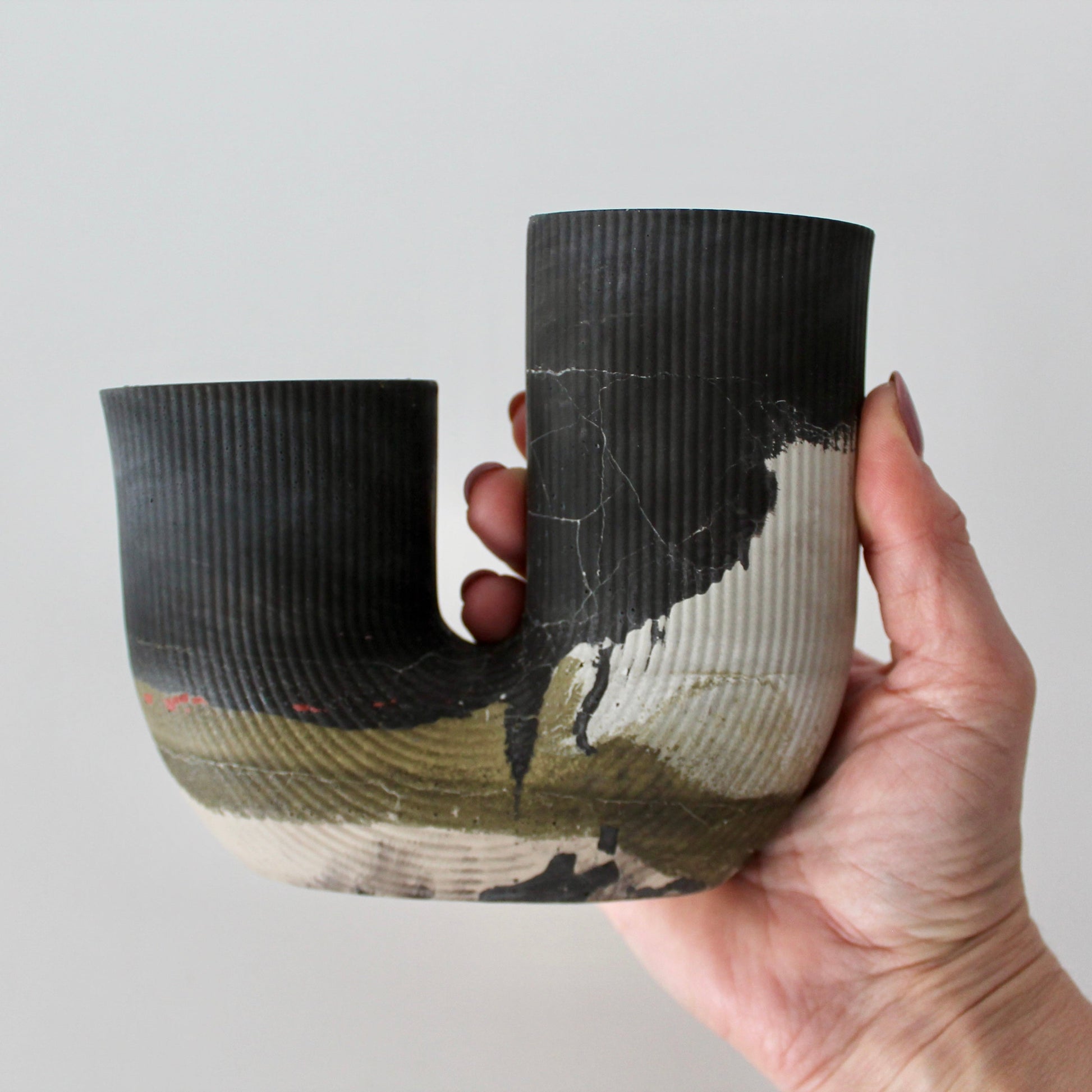 Hand holding a black and white cement vessel against a plain background