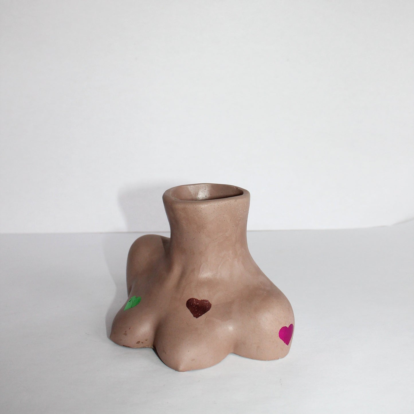 concrete breast shaped vase with multiple colored hearts on a white background