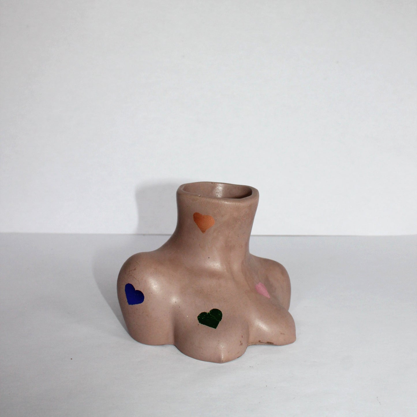 concrete vase shaped like a torso with colored heart designs on a white background